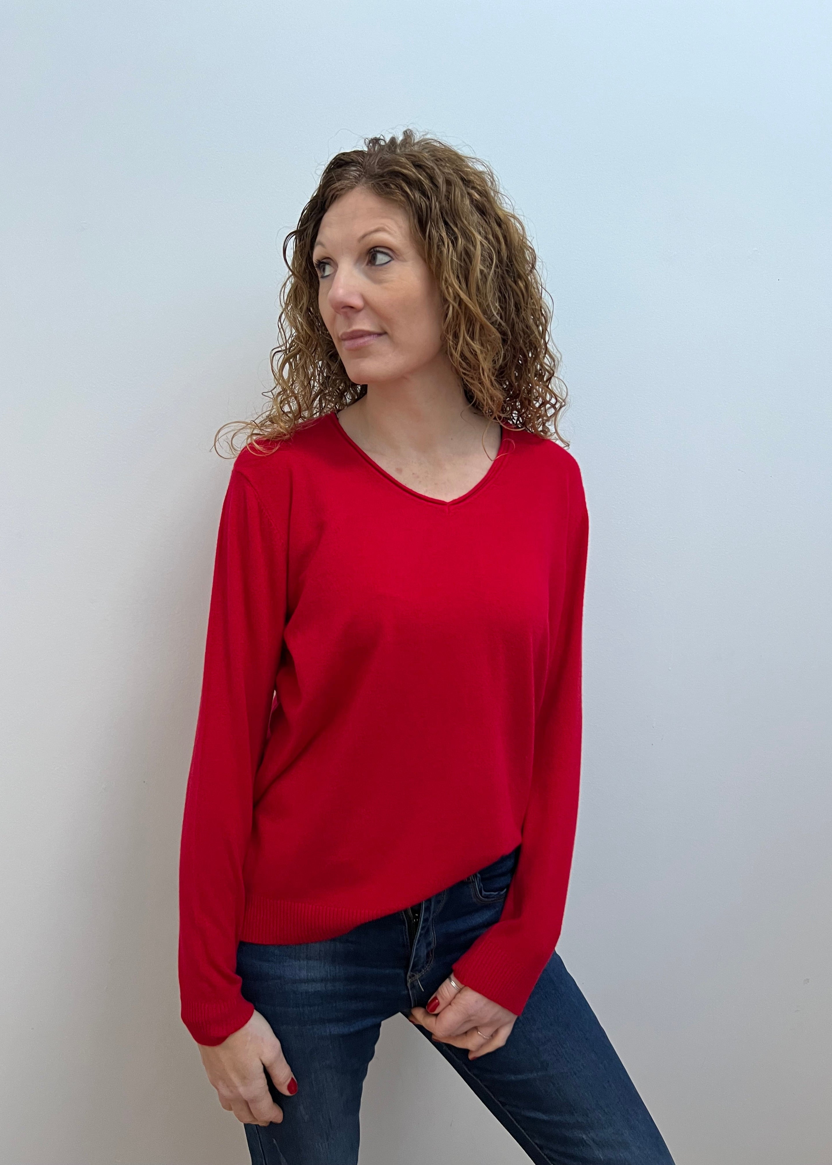 A woman wearing a red V-neck jumper and blue jeans.
