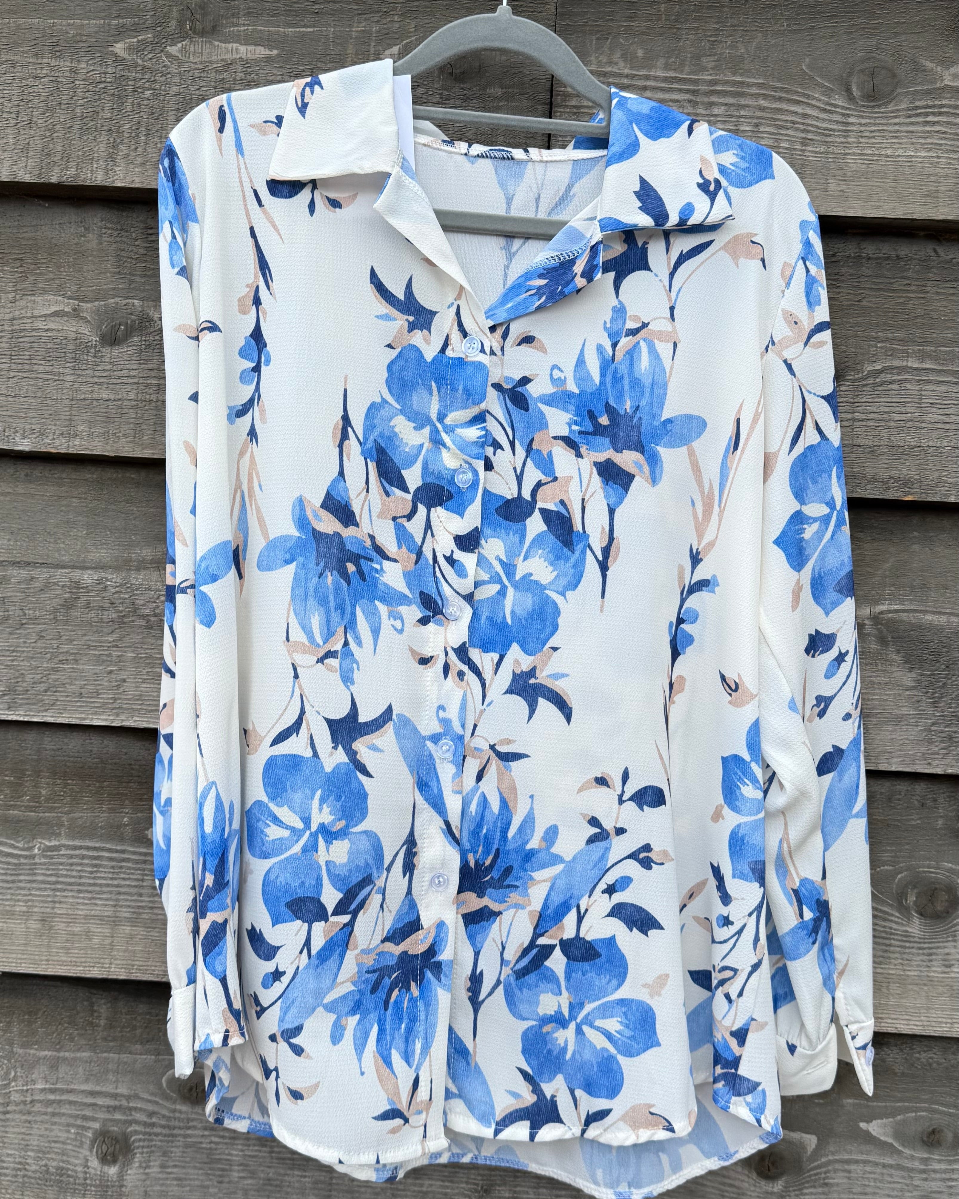 White blouse with blue floral pattern on a hanger against a wooden background