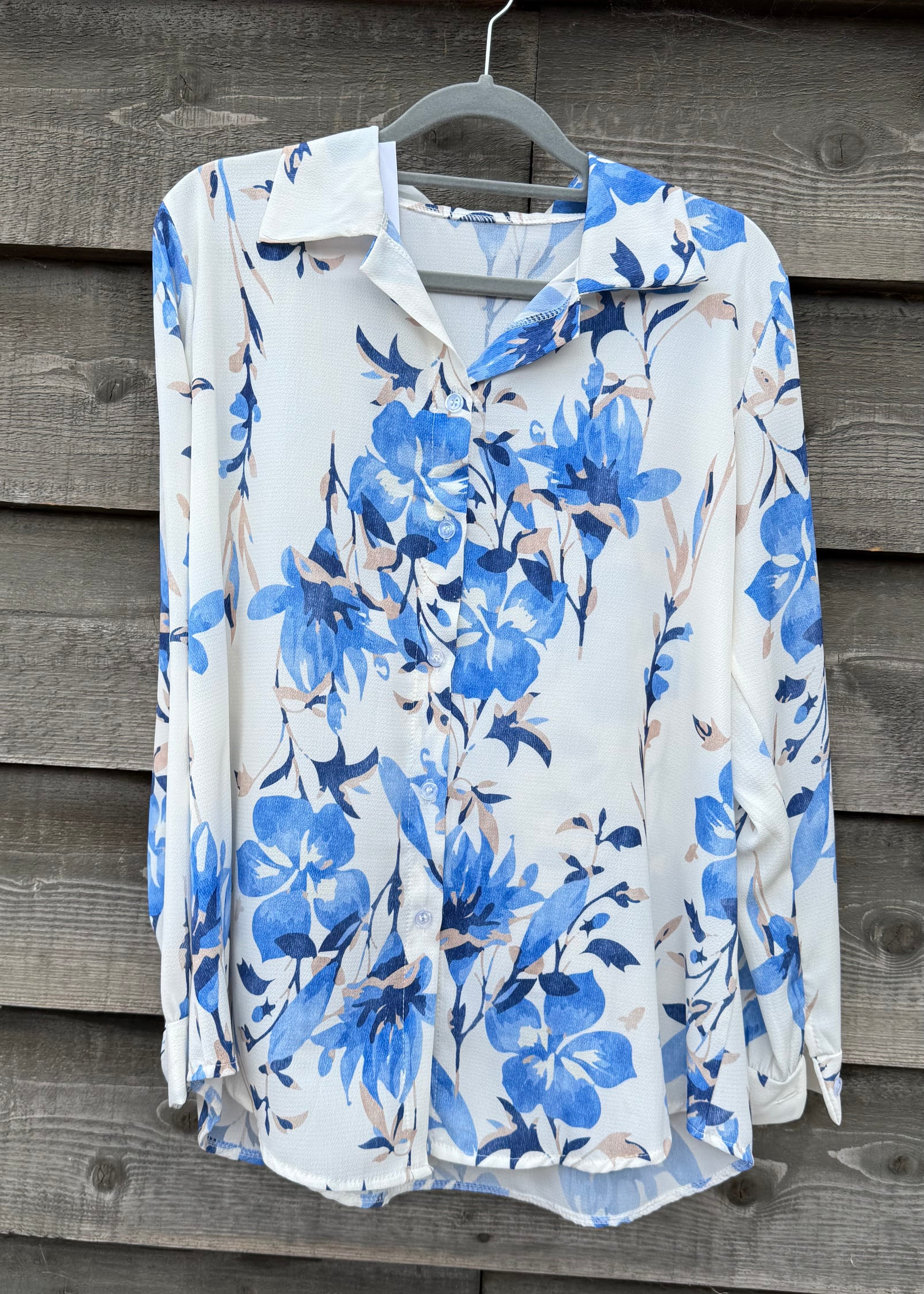 White blouse with blue floral pattern on a hanger against a wooden background