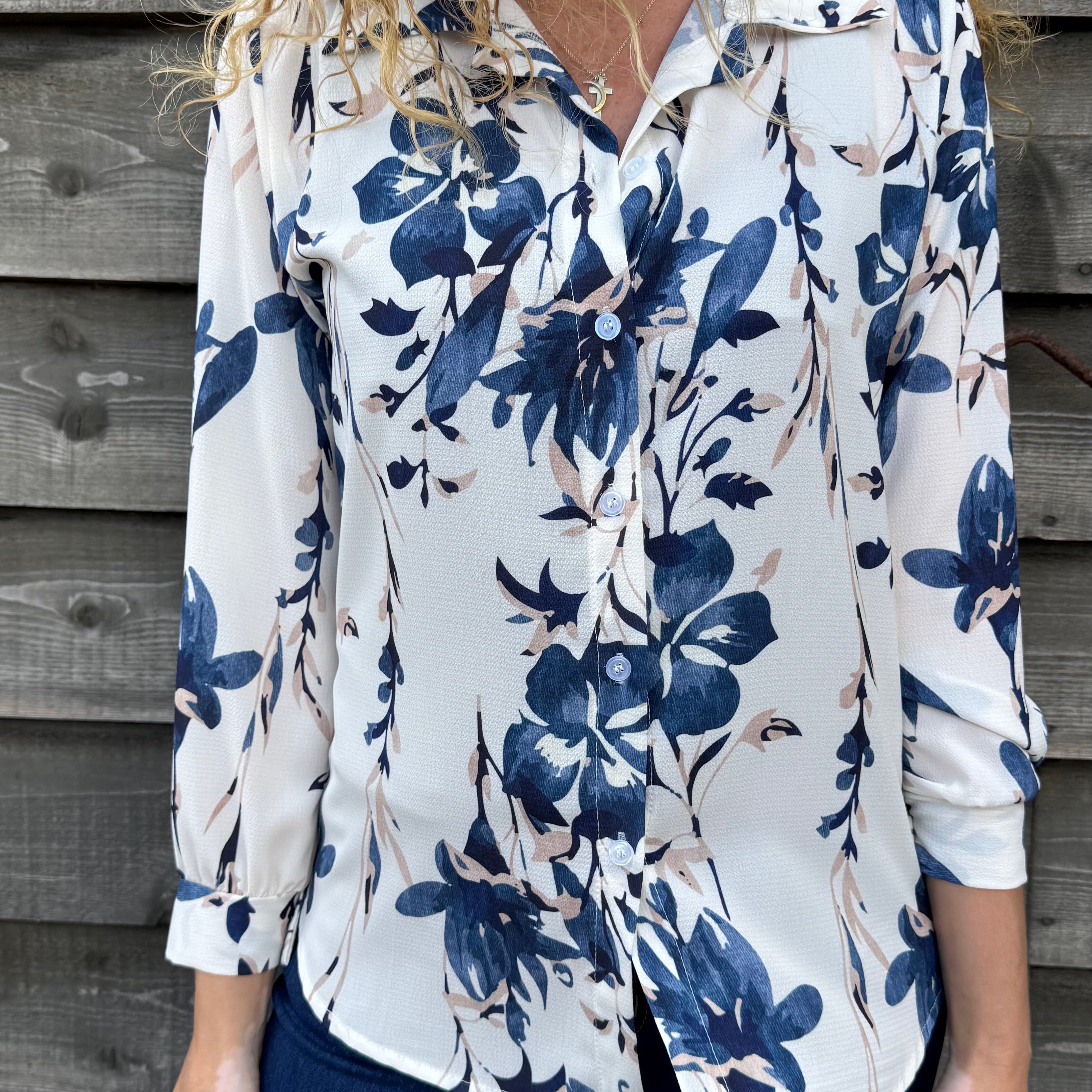Woman wearing a white blouse with blue floral pattern against a wooden wall.