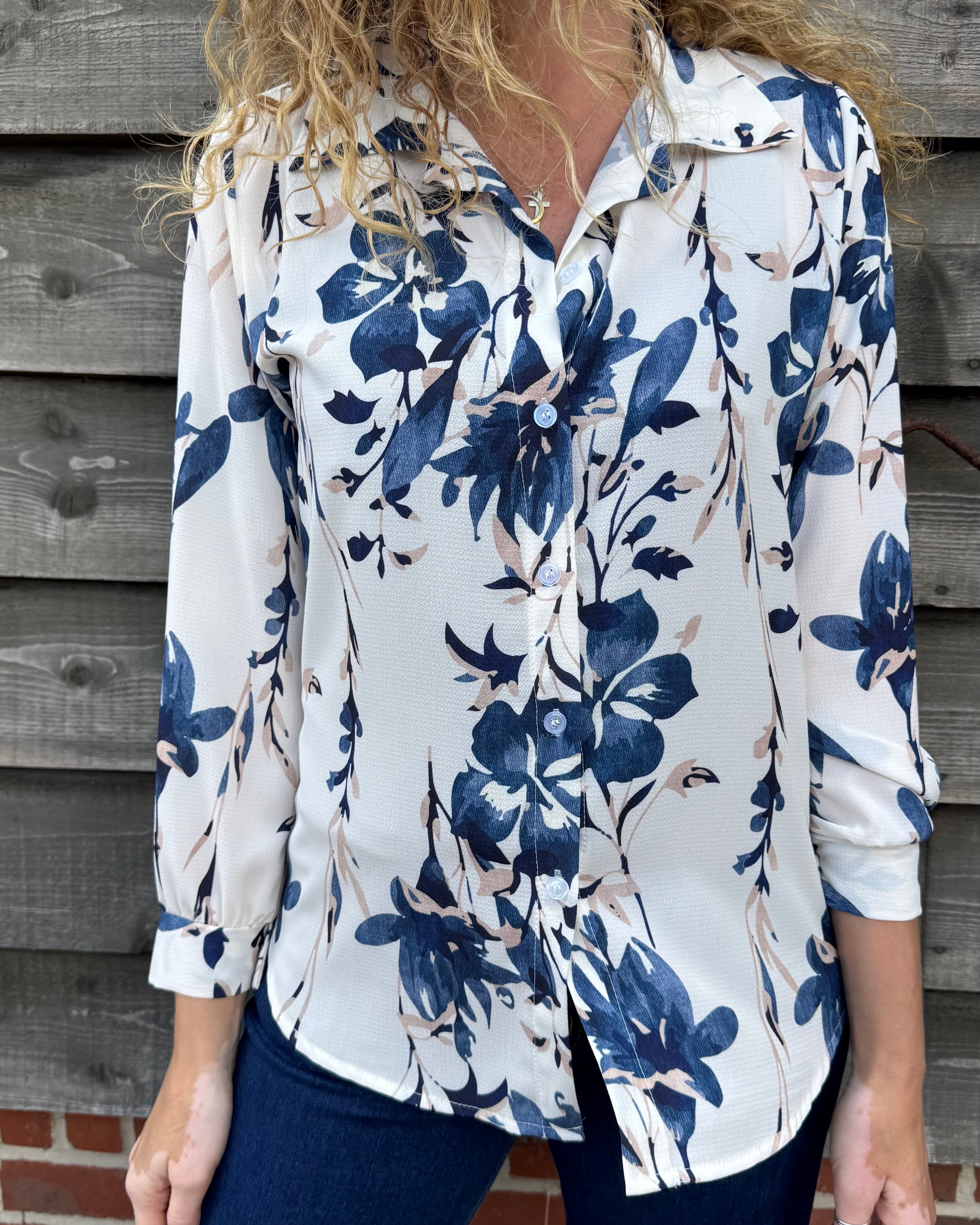 Woman wearing a white blouse with blue floral pattern against a wooden wall.
