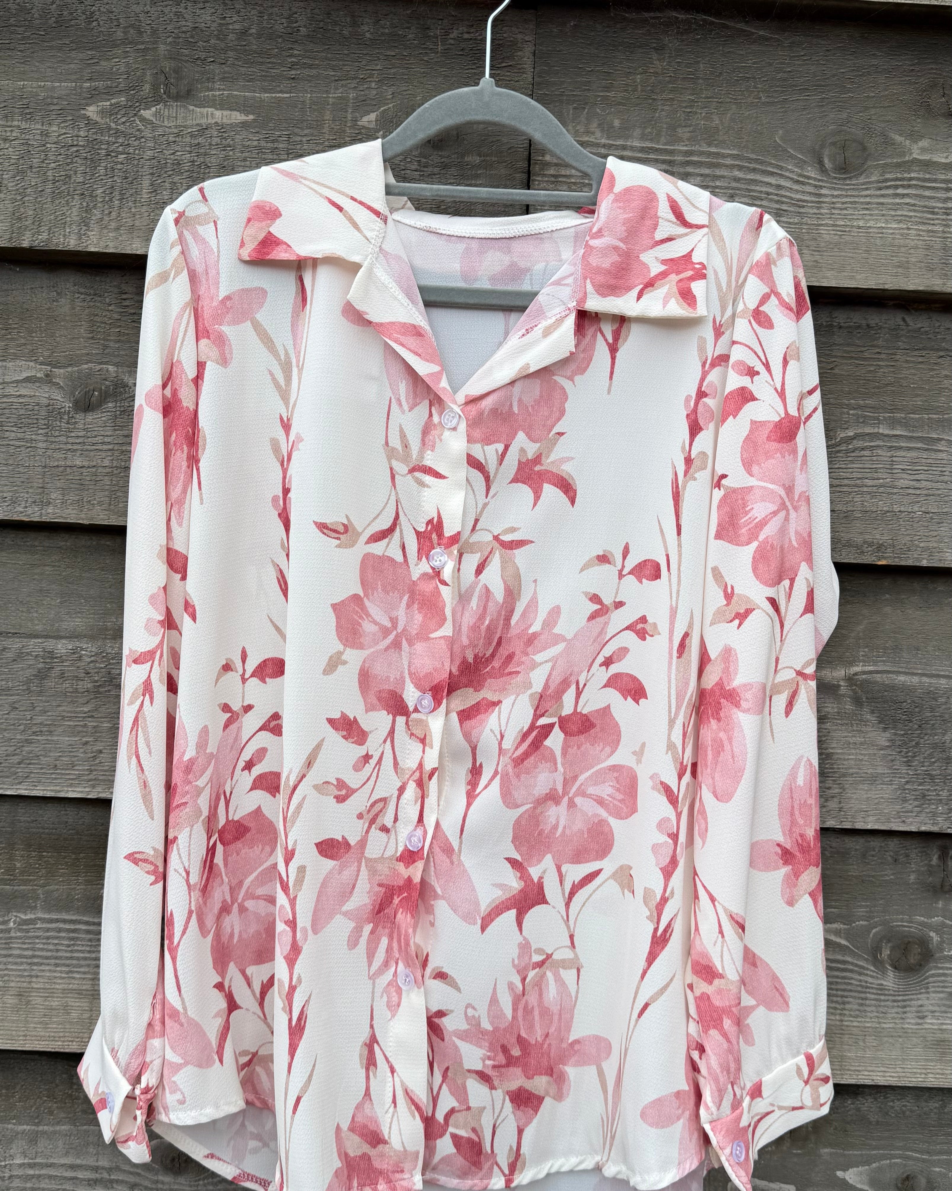 Floral blouse with pink flowers on a hanger against a wooden wall