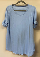 A woman wearing a light blue, long-sleeved cotton top with curved raw edges, in a loose fit style.