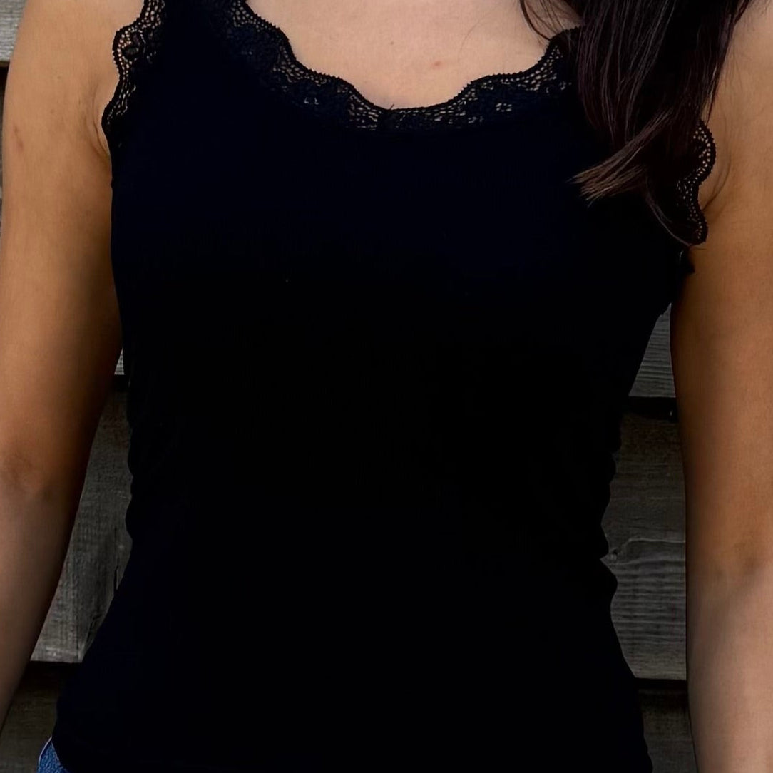 Woman wearing a black top and denim shorts standing against a wooden wall.