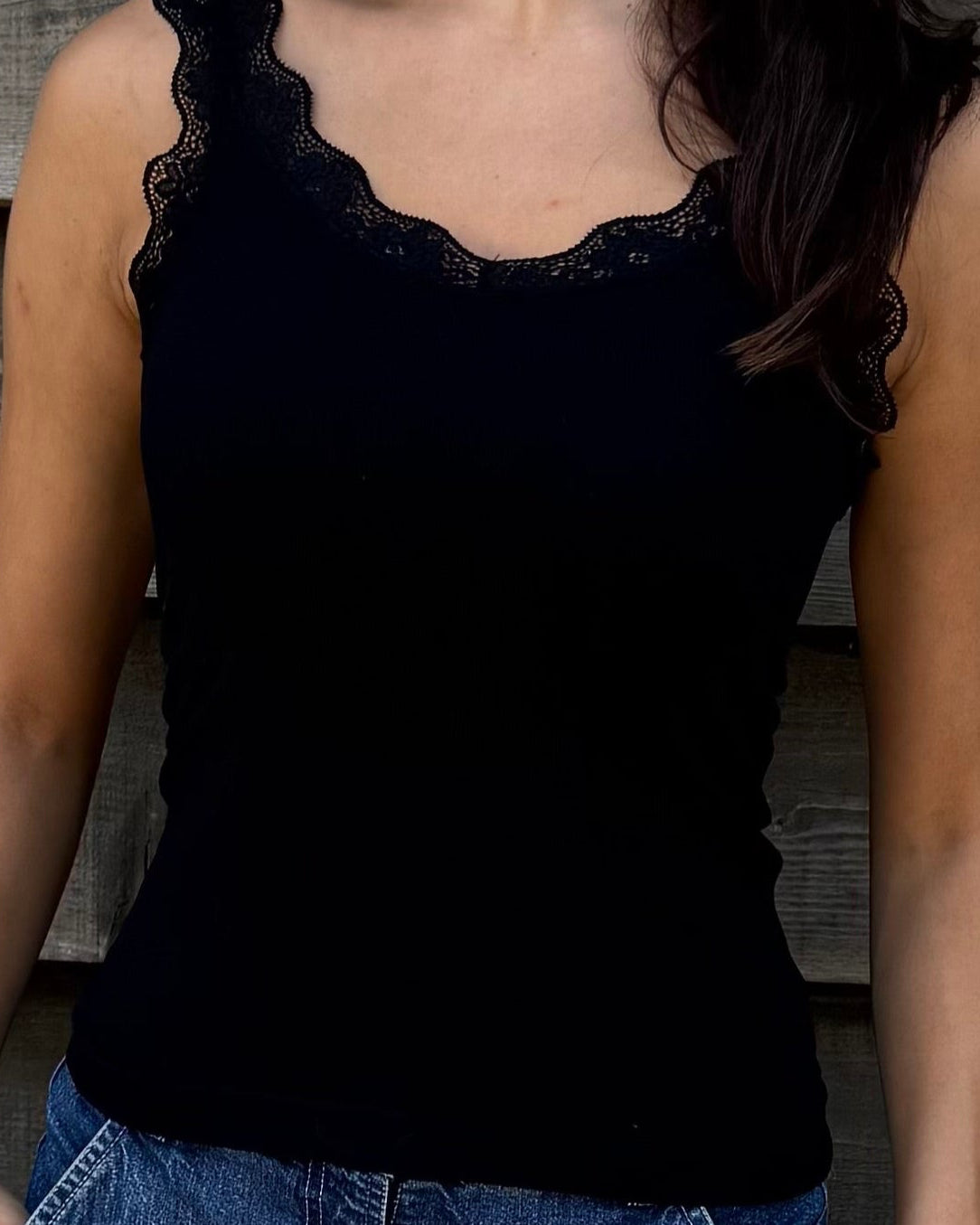 Woman wearing a black top and denim shorts standing against a wooden wall.