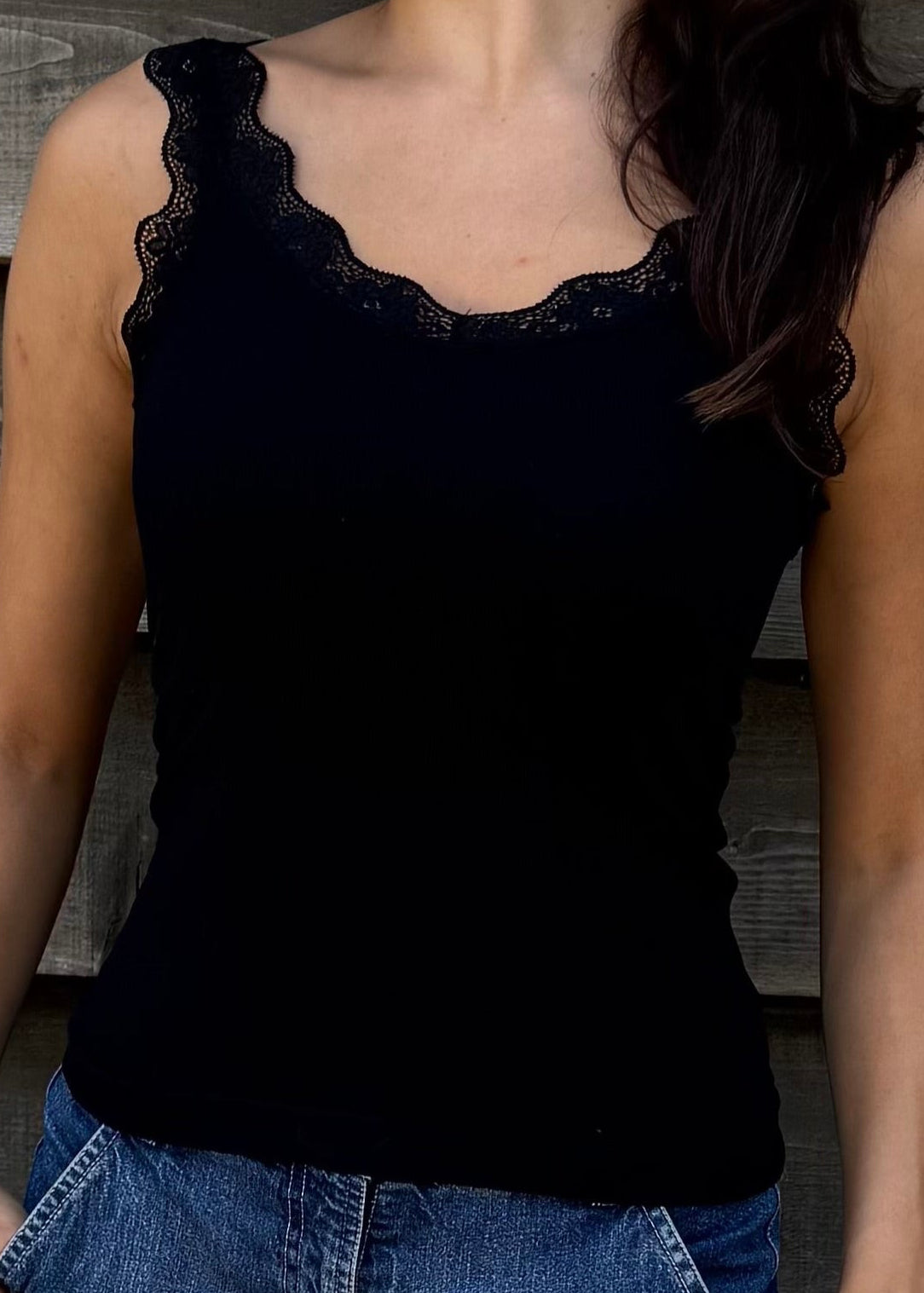 Woman wearing a black top and denim shorts standing against a wooden wall.