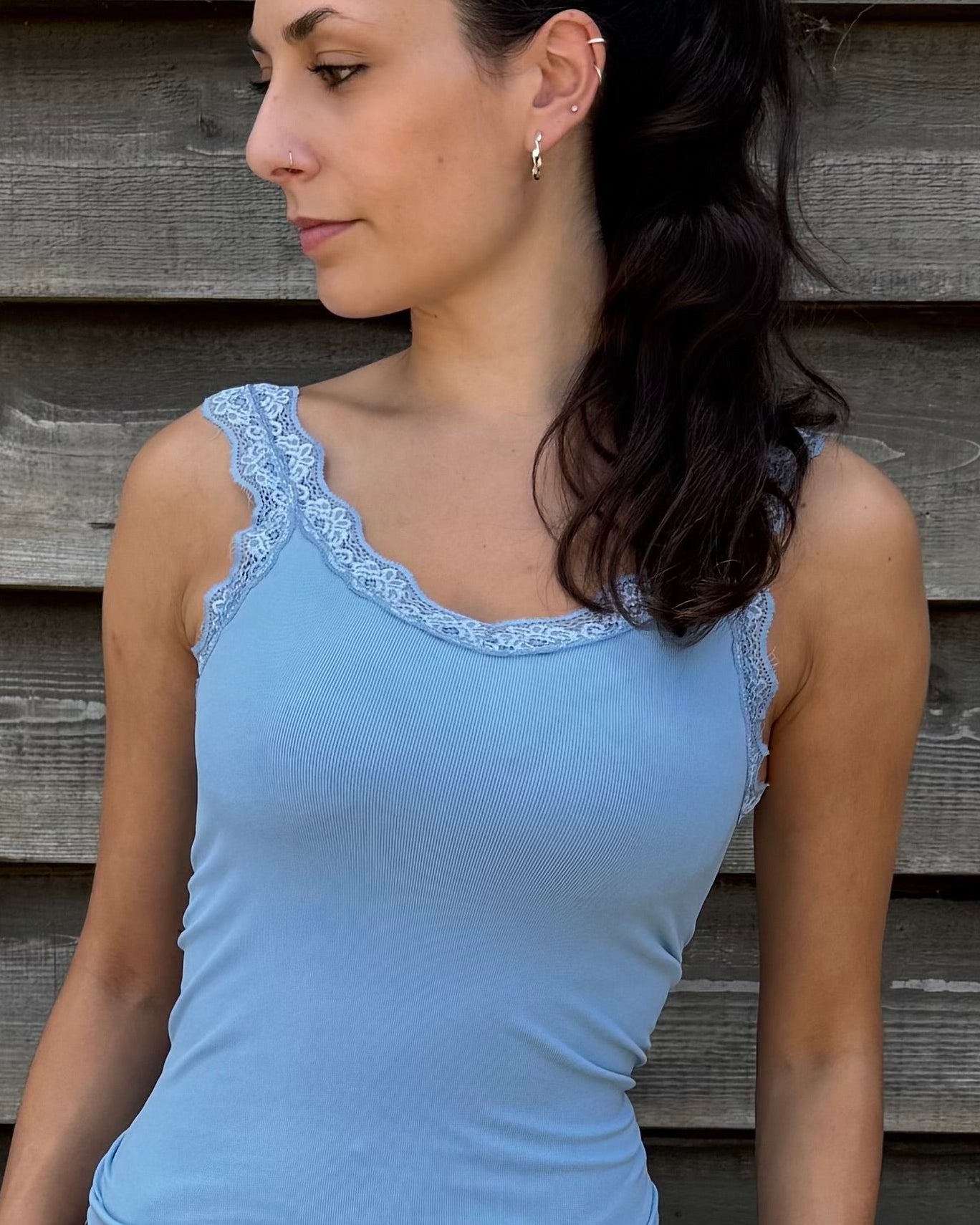 Woman wearing a blue tank top and denim shorts standing against a wooden wall.