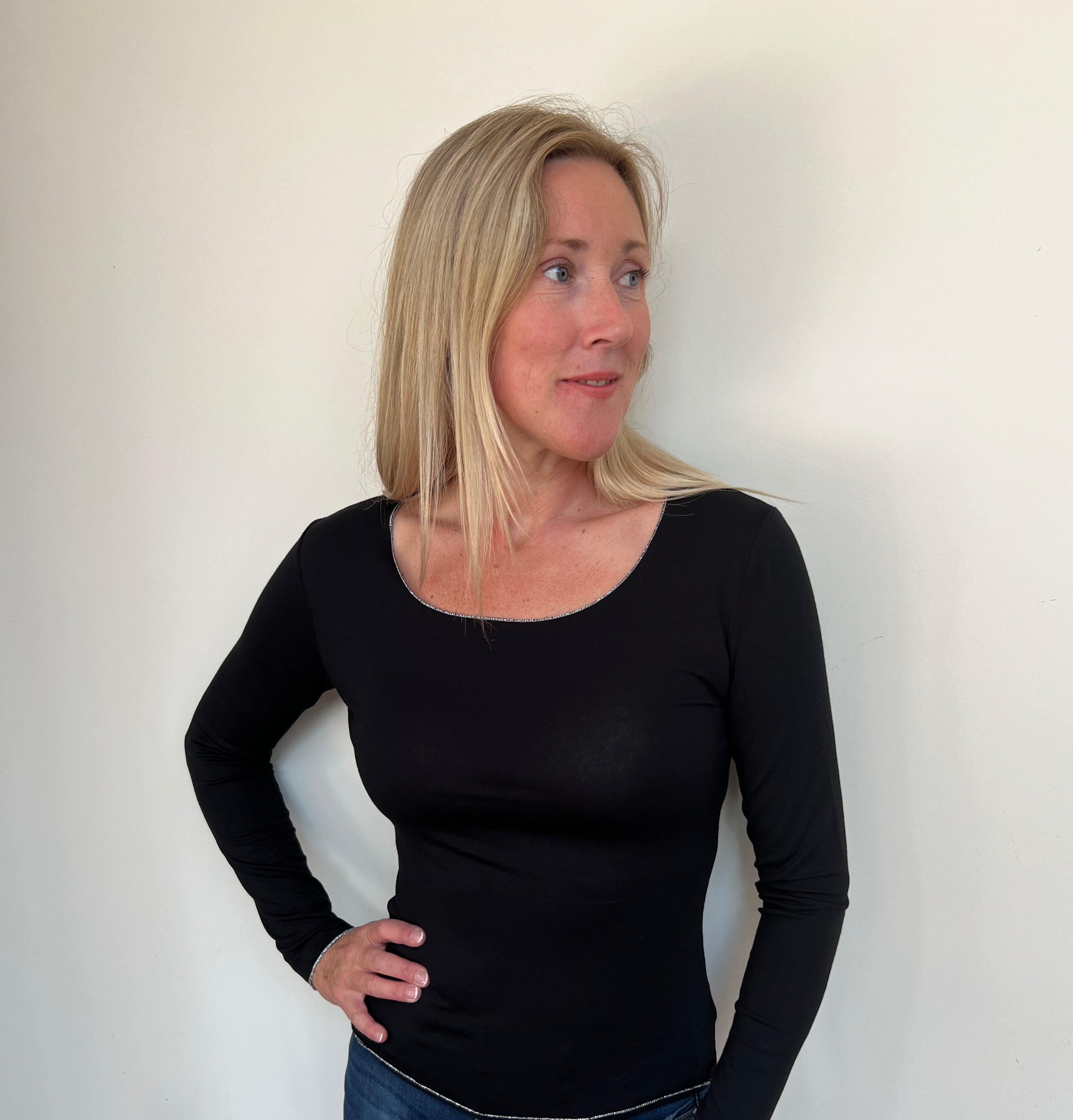 A woman wearing a black long-sleeved top with a round neckline, paired with blue jeans.