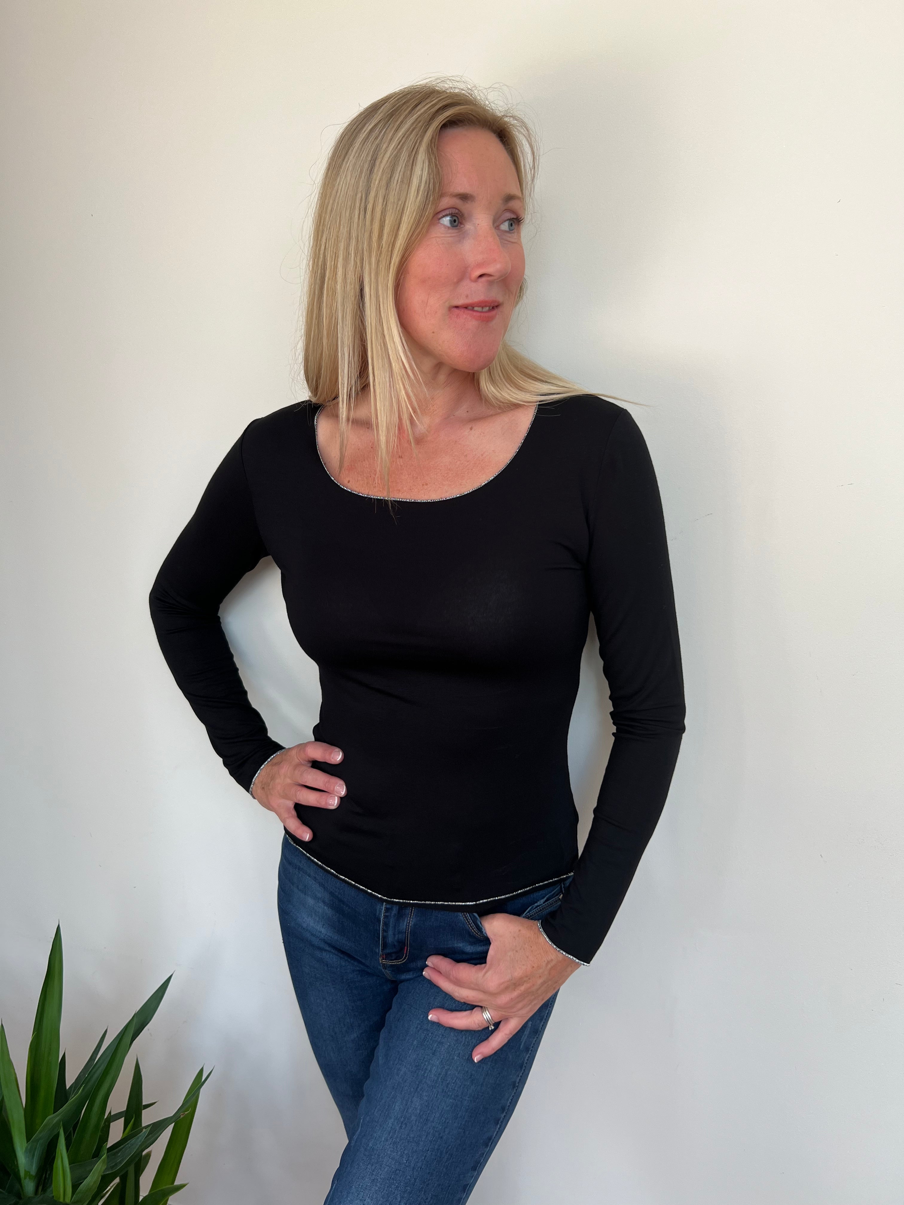A woman wearing a black long-sleeved top with a round neckline, paired with blue jeans.