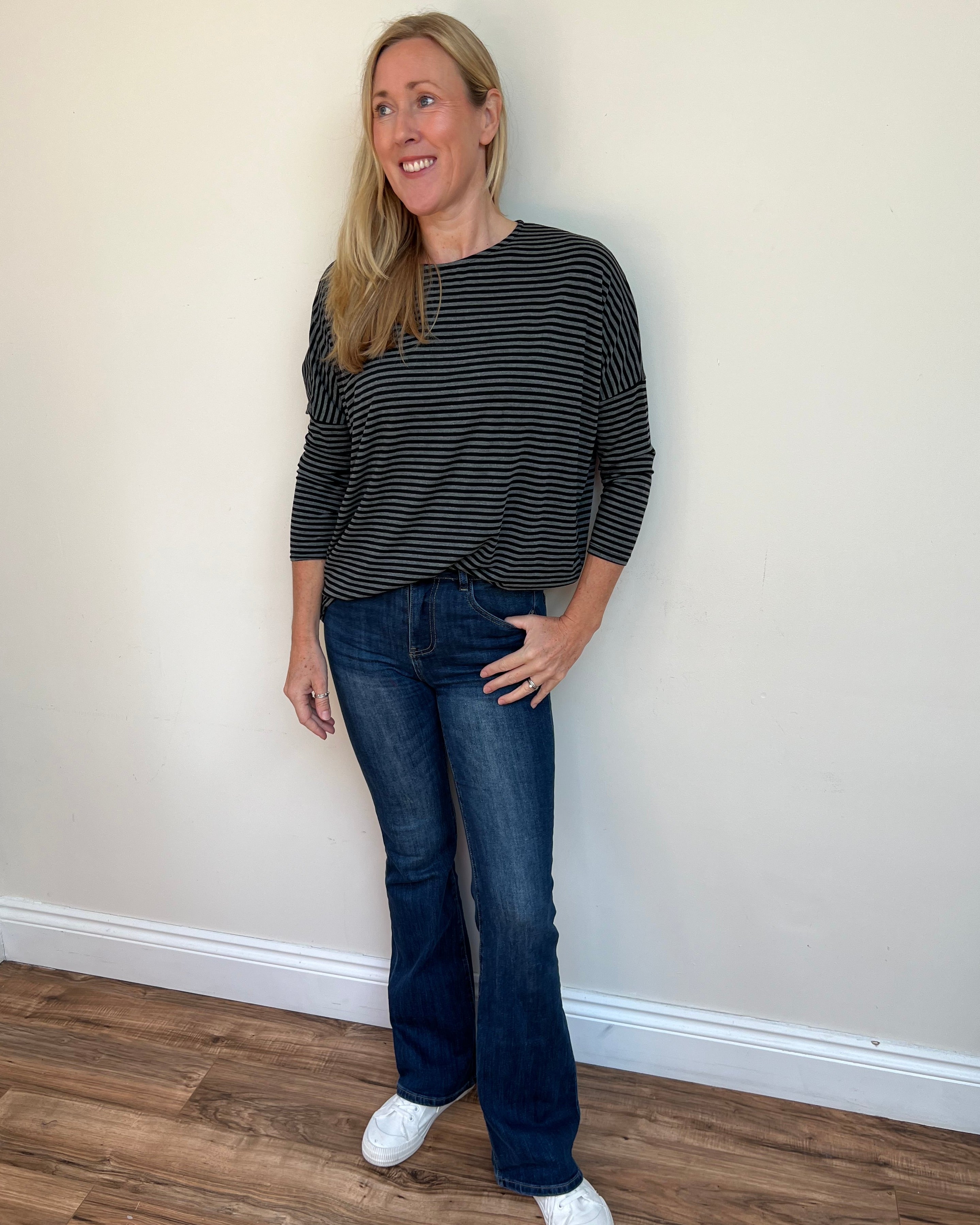 Woman wearing a black and white striped shirt and blue jeans standing against a plain wall.
