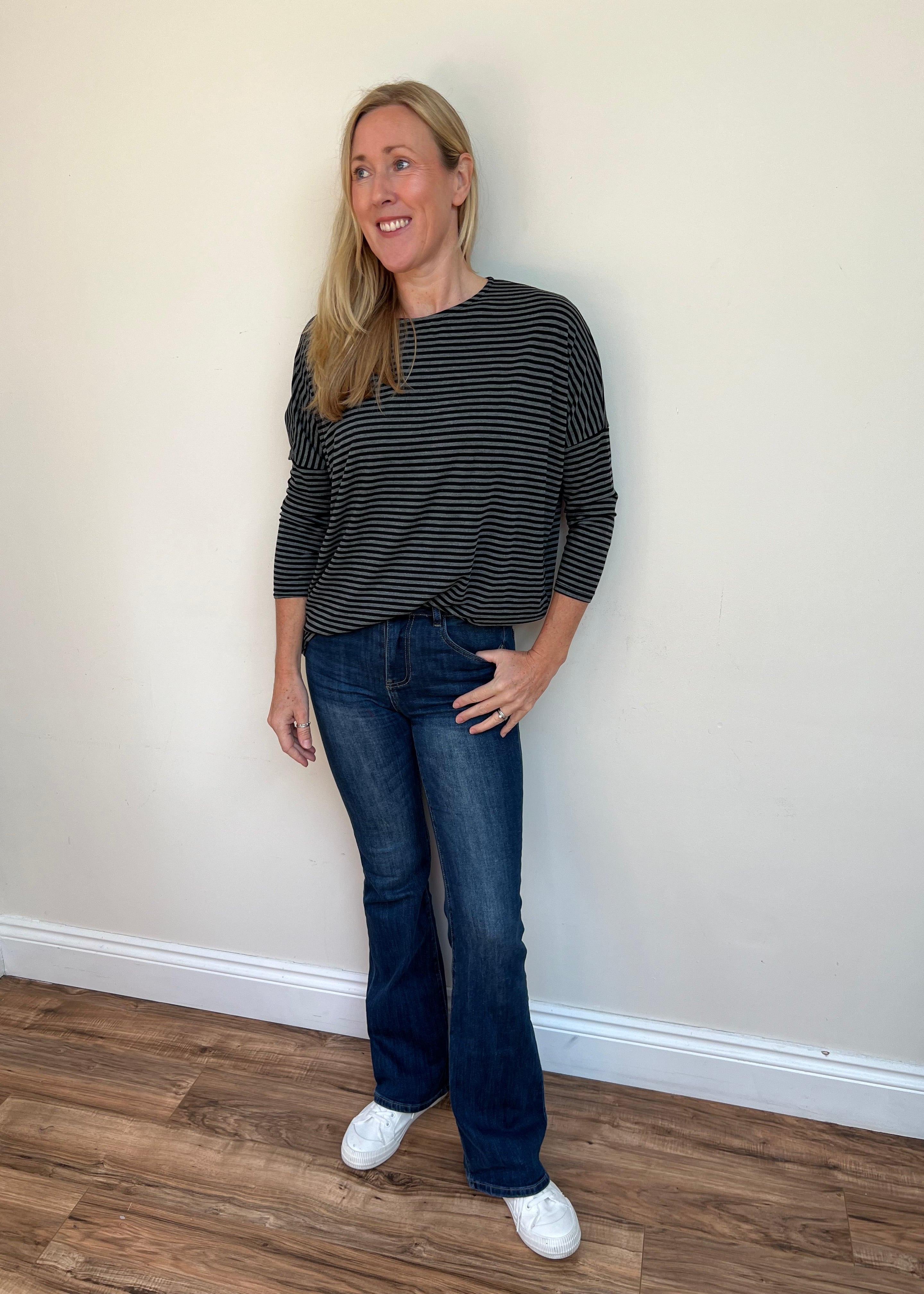 Woman wearing a black and white striped shirt and blue jeans standing against a plain wall.
