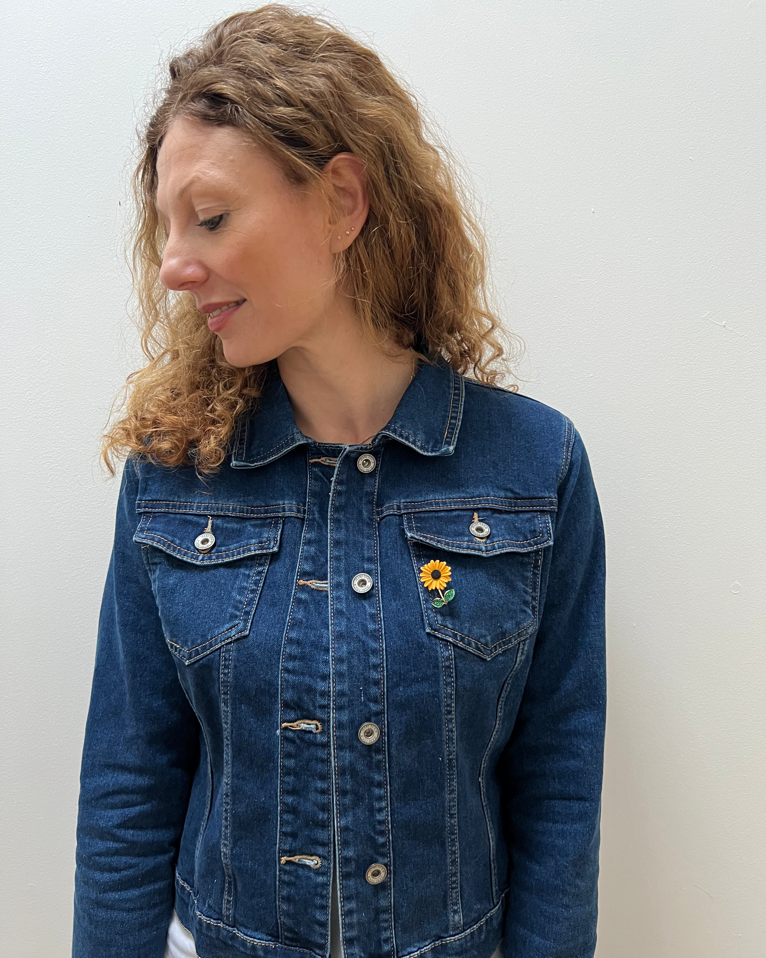 A person wearing a blue denim jacket with a sunflower brooch on the lapel.