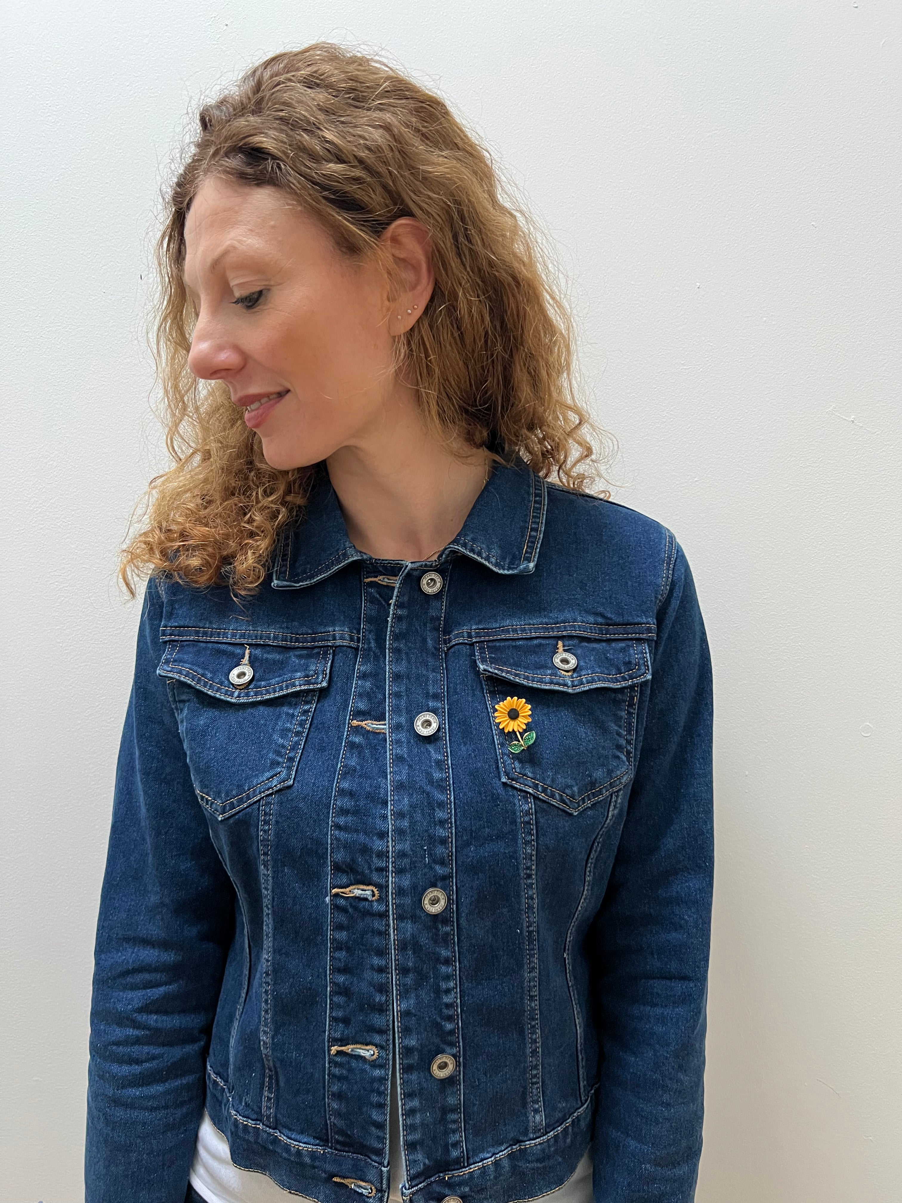 A person wearing a blue denim jacket with a sunflower brooch on the lapel.