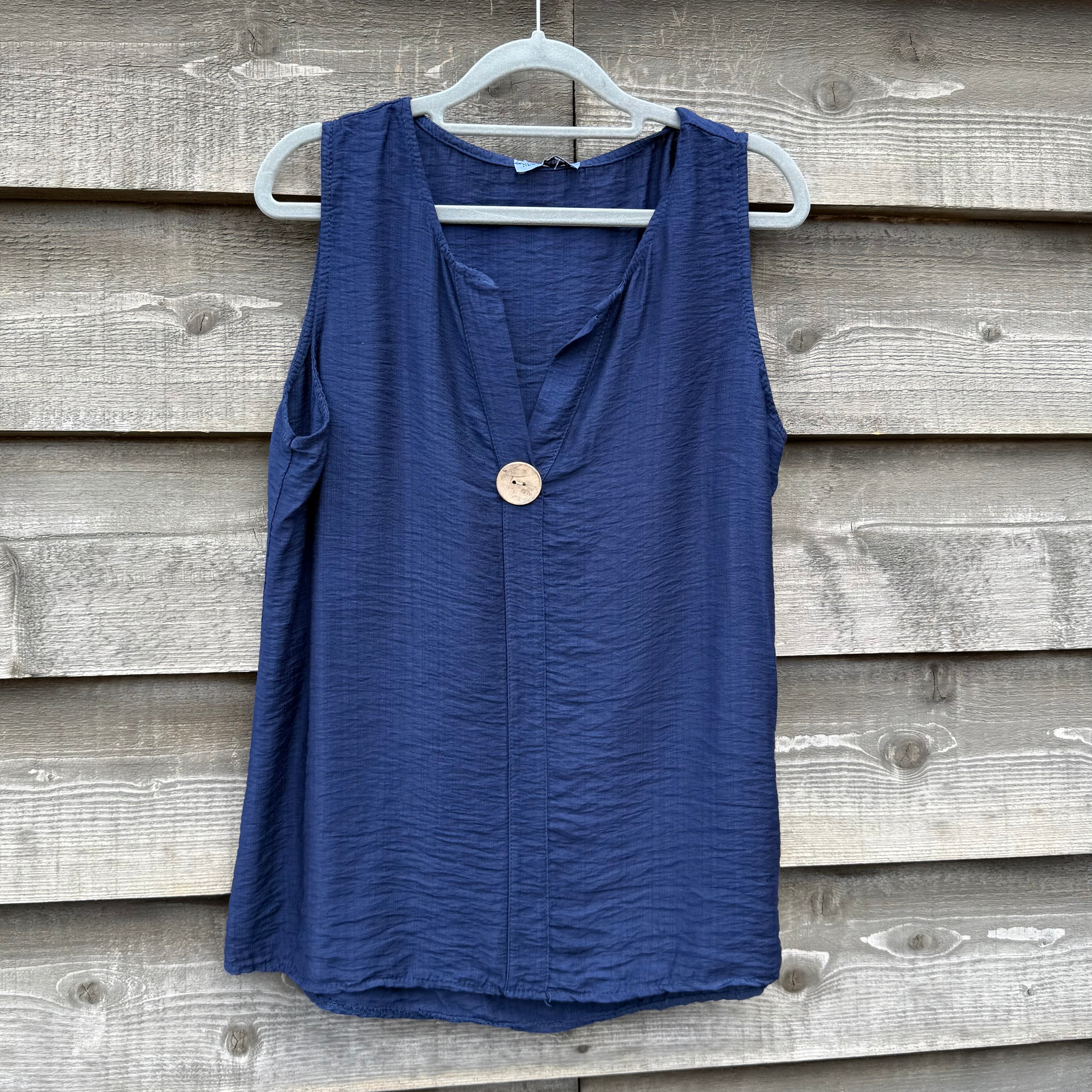 Blue sleeveless top on a hanger against a wooden wall