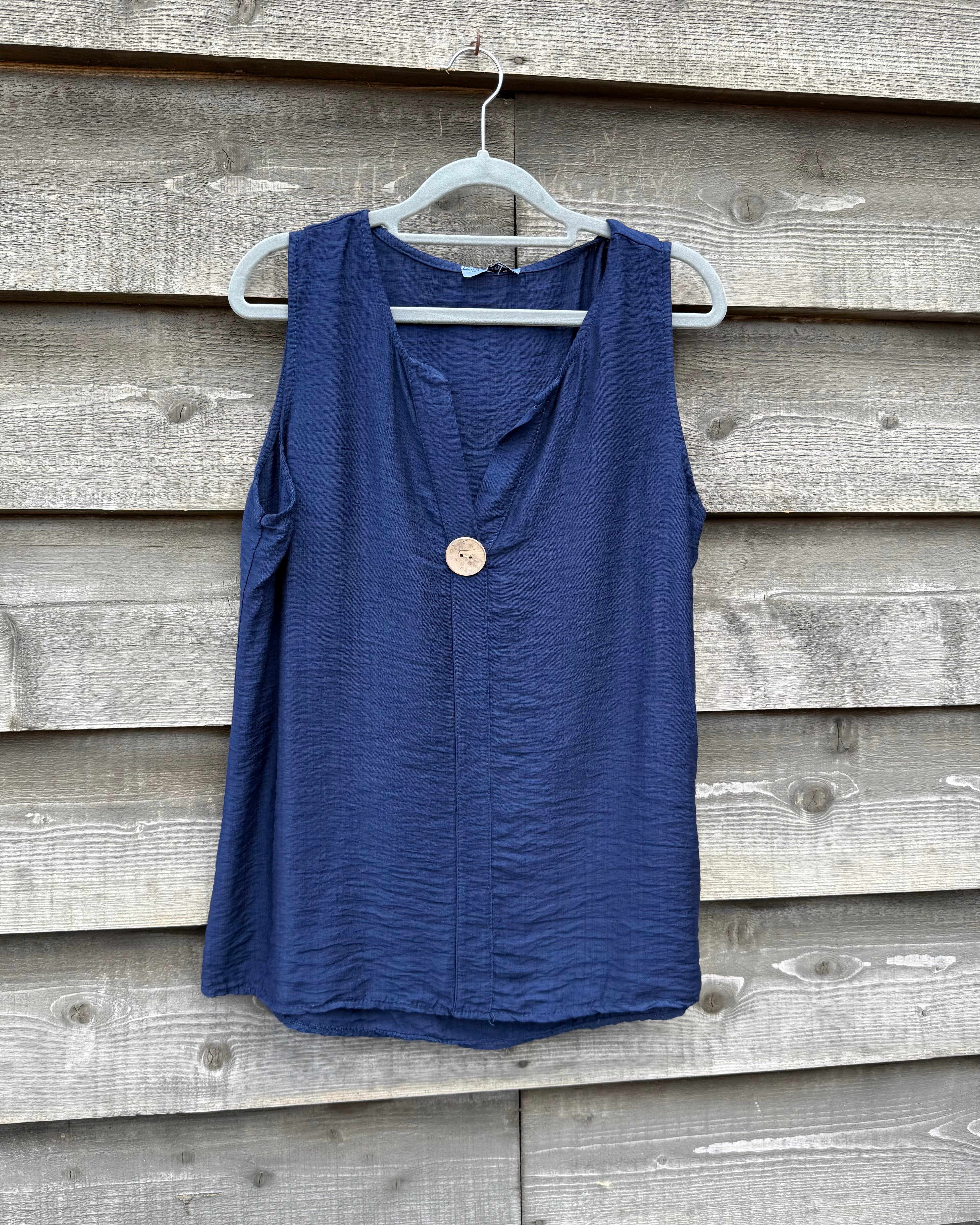 Blue sleeveless top on a hanger against a wooden wall