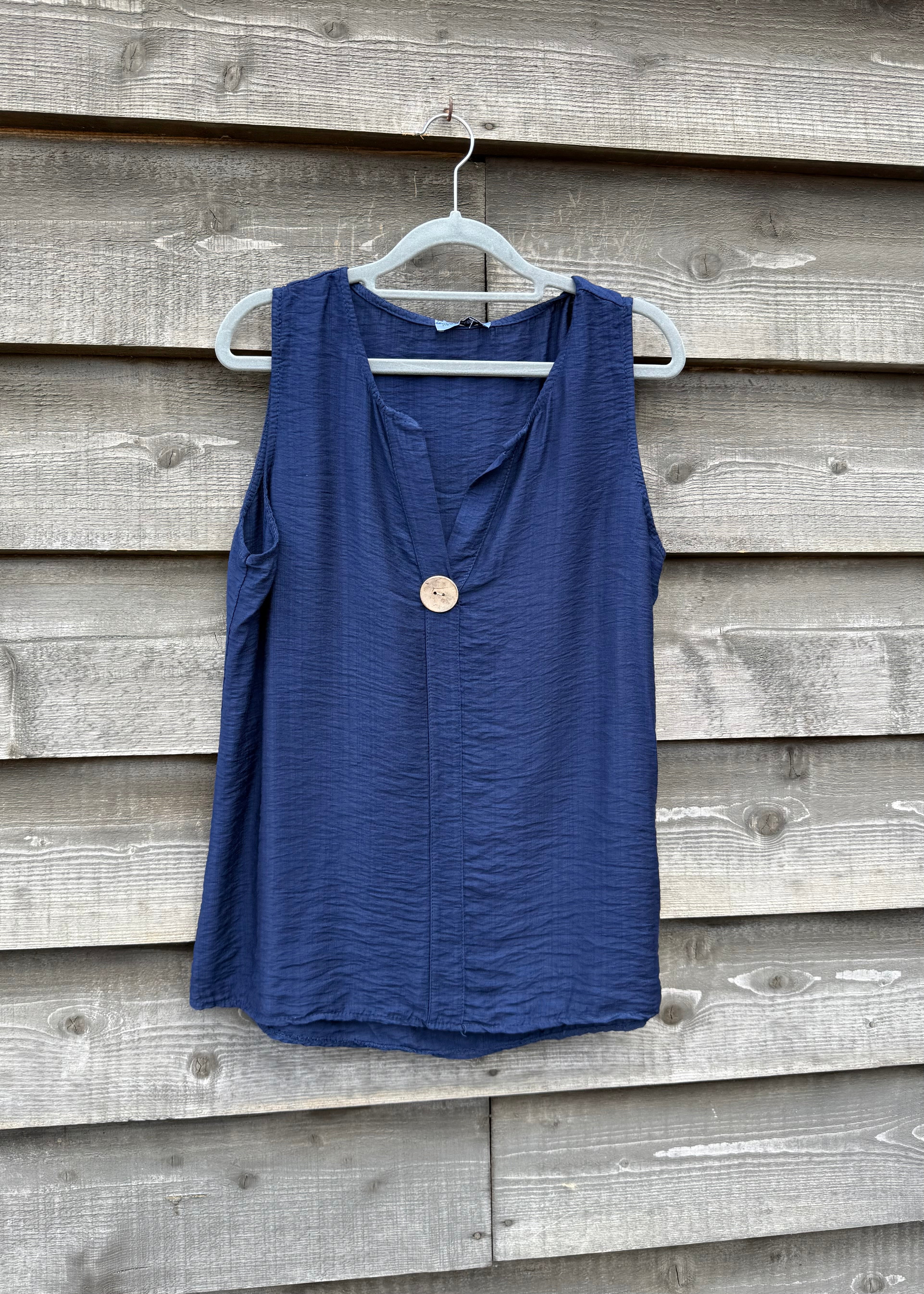 Blue sleeveless top on a hanger against a wooden wall
