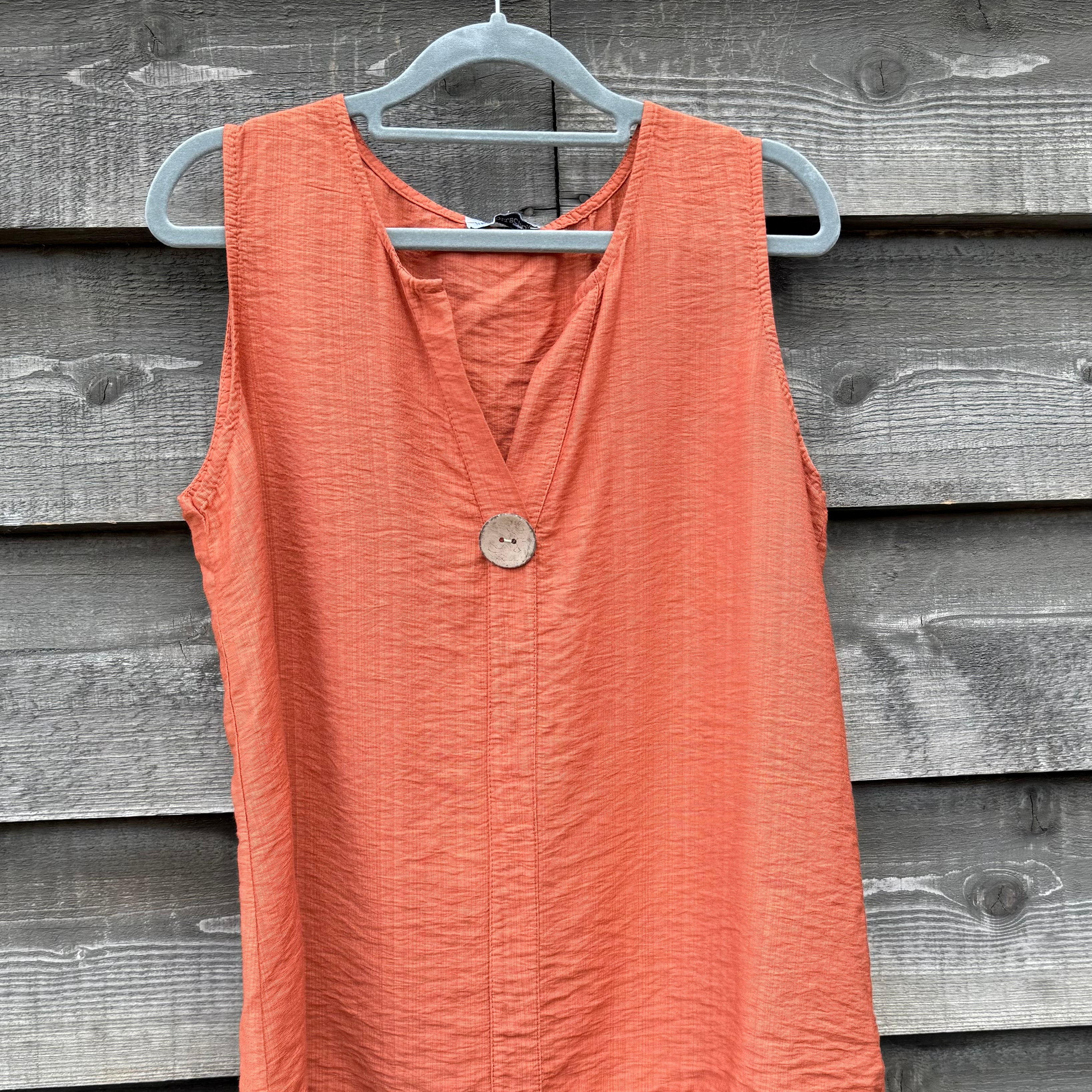 Coral sleeveless top on a hanger against a wooden background