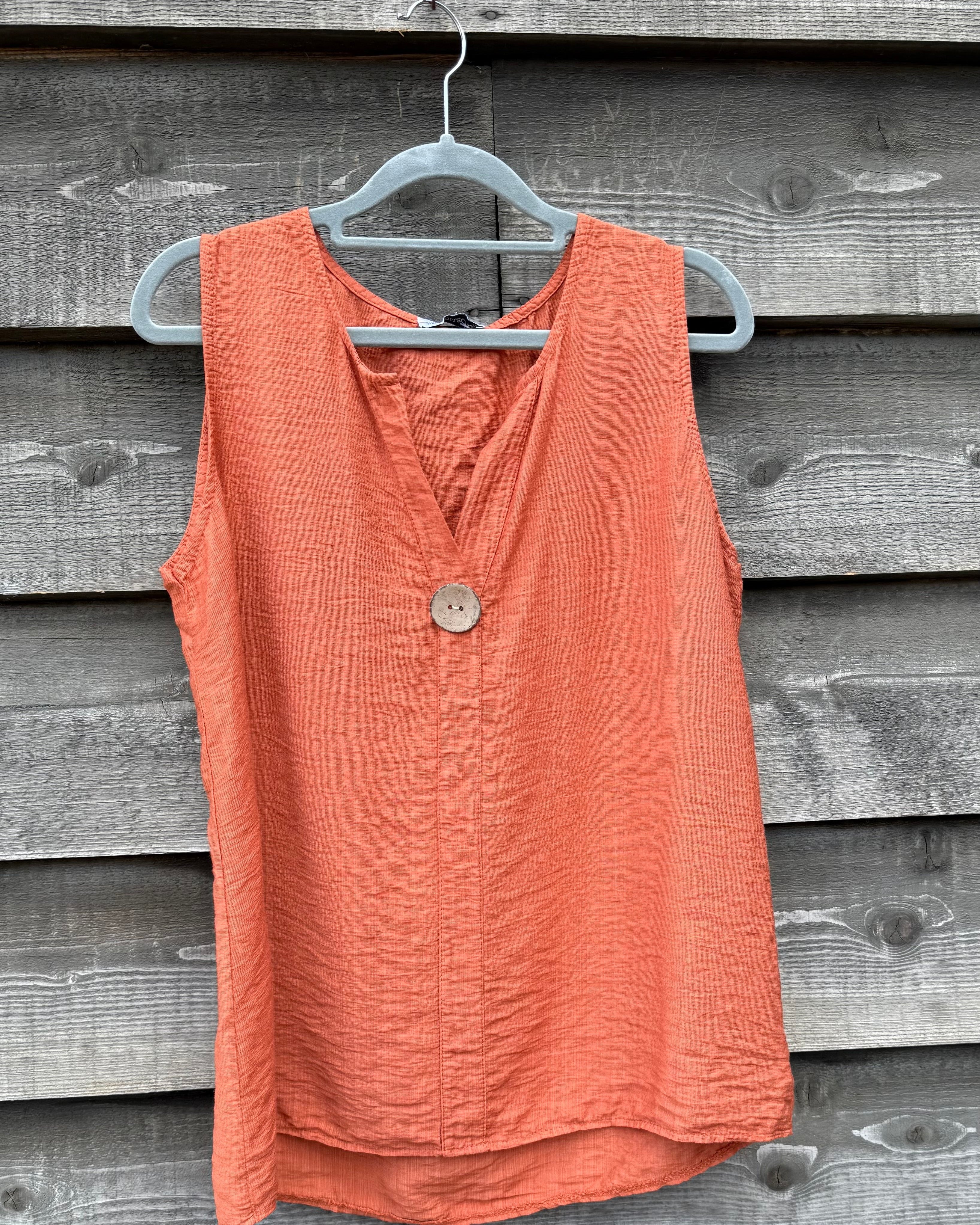 Coral sleeveless top on a hanger against a wooden background