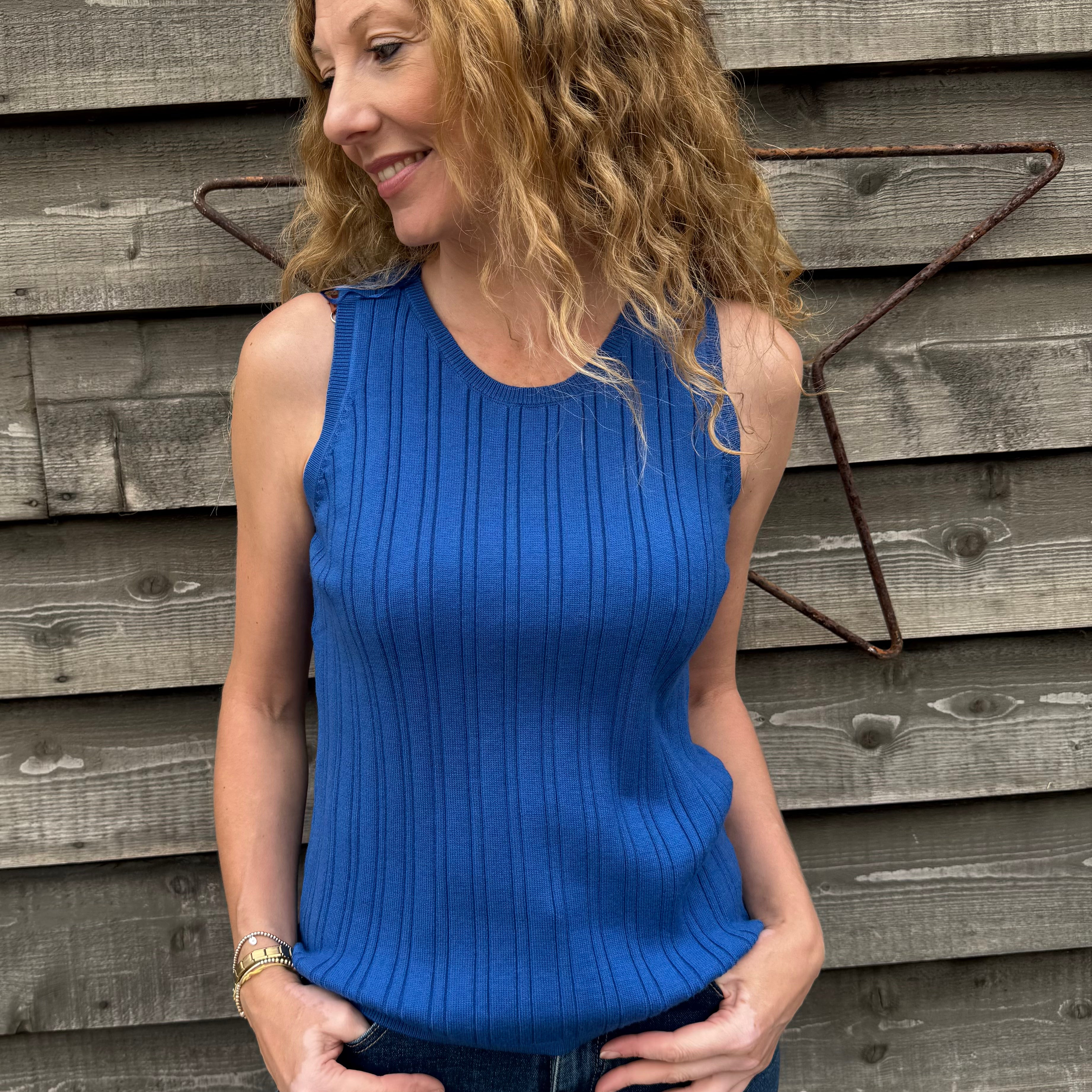Woman wearing a blue sleeveless top standing against a wooden wall.