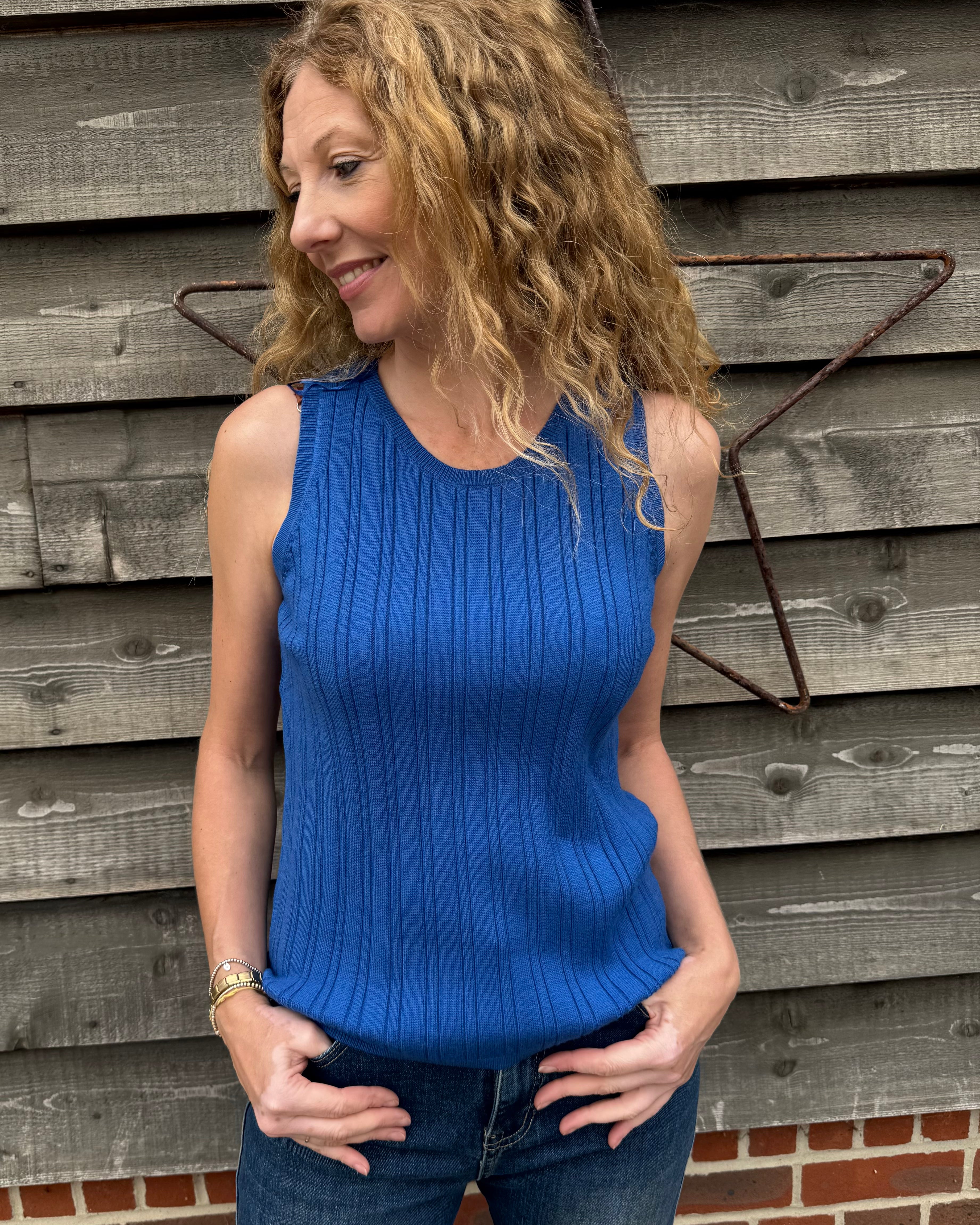 Woman wearing a blue sleeveless top standing against a wooden wall.
