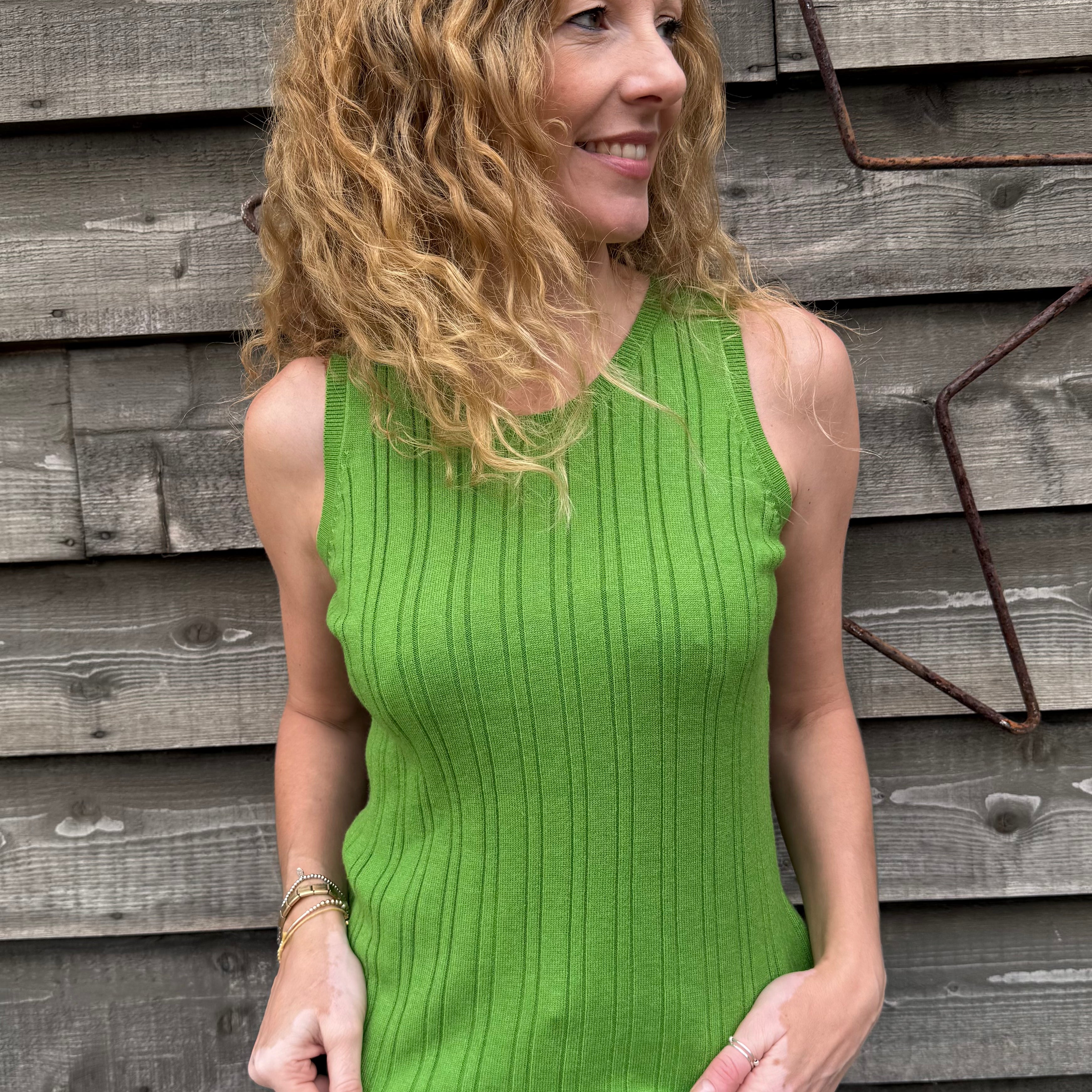 Woman wearing a green sleeveless sweater against a wooden wall.