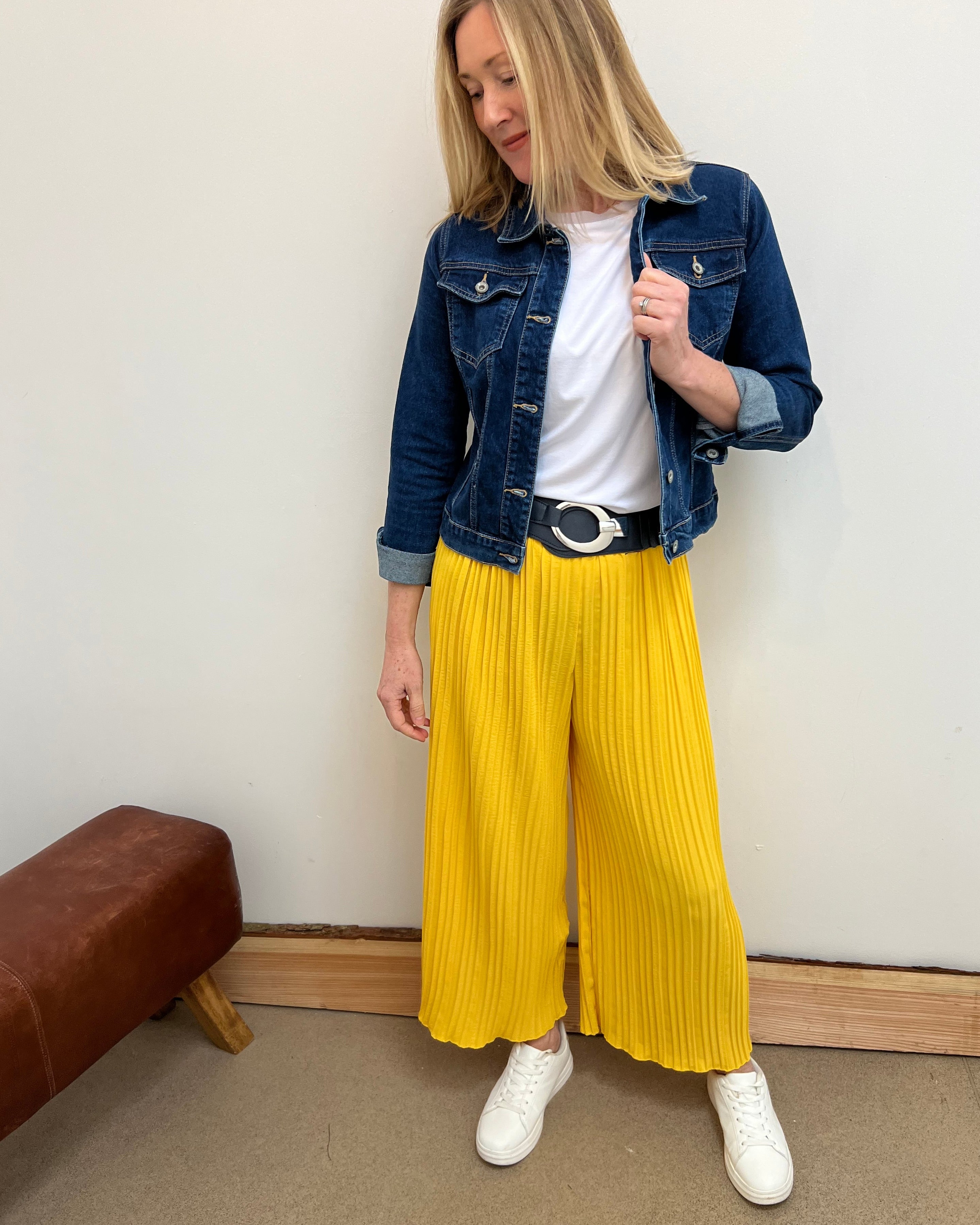 A person wearing yellow pleated trousers with a denim jacket and white shoes.
