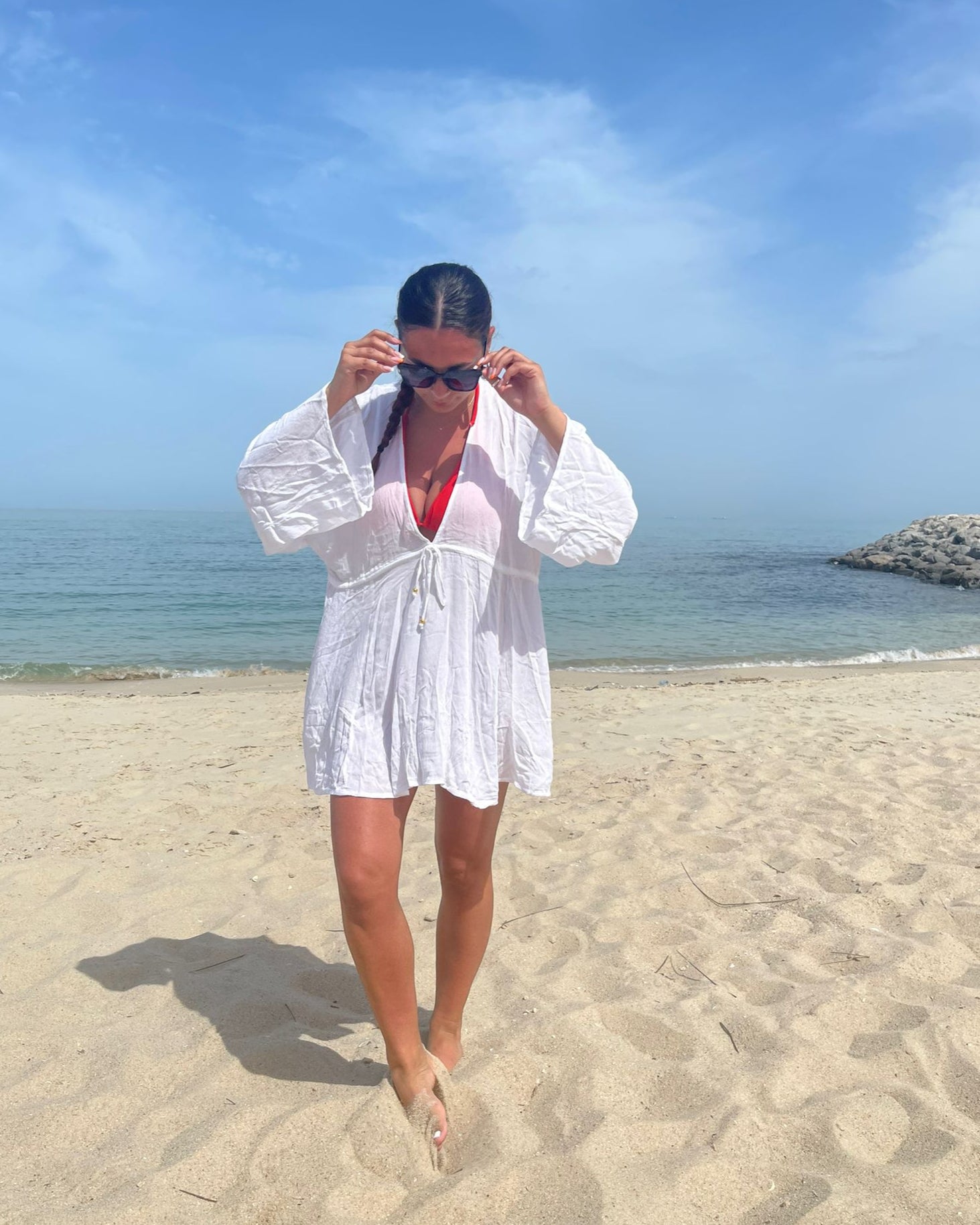 A person standing on a beach wearing a white viscose kaftan dress with 3/4 length sleeves.