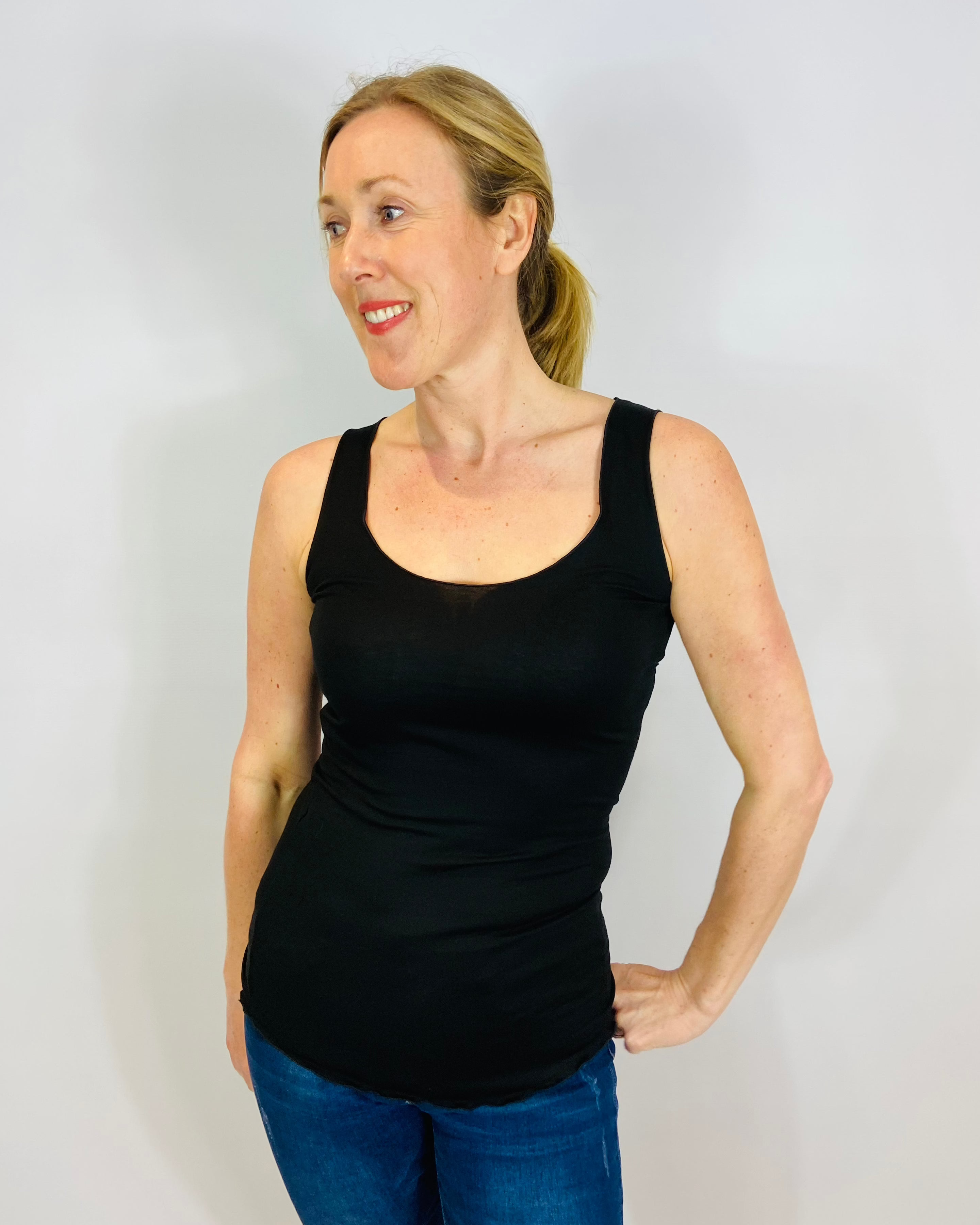 A woman wearing a black fitted tank top vest, standing against a plain background.