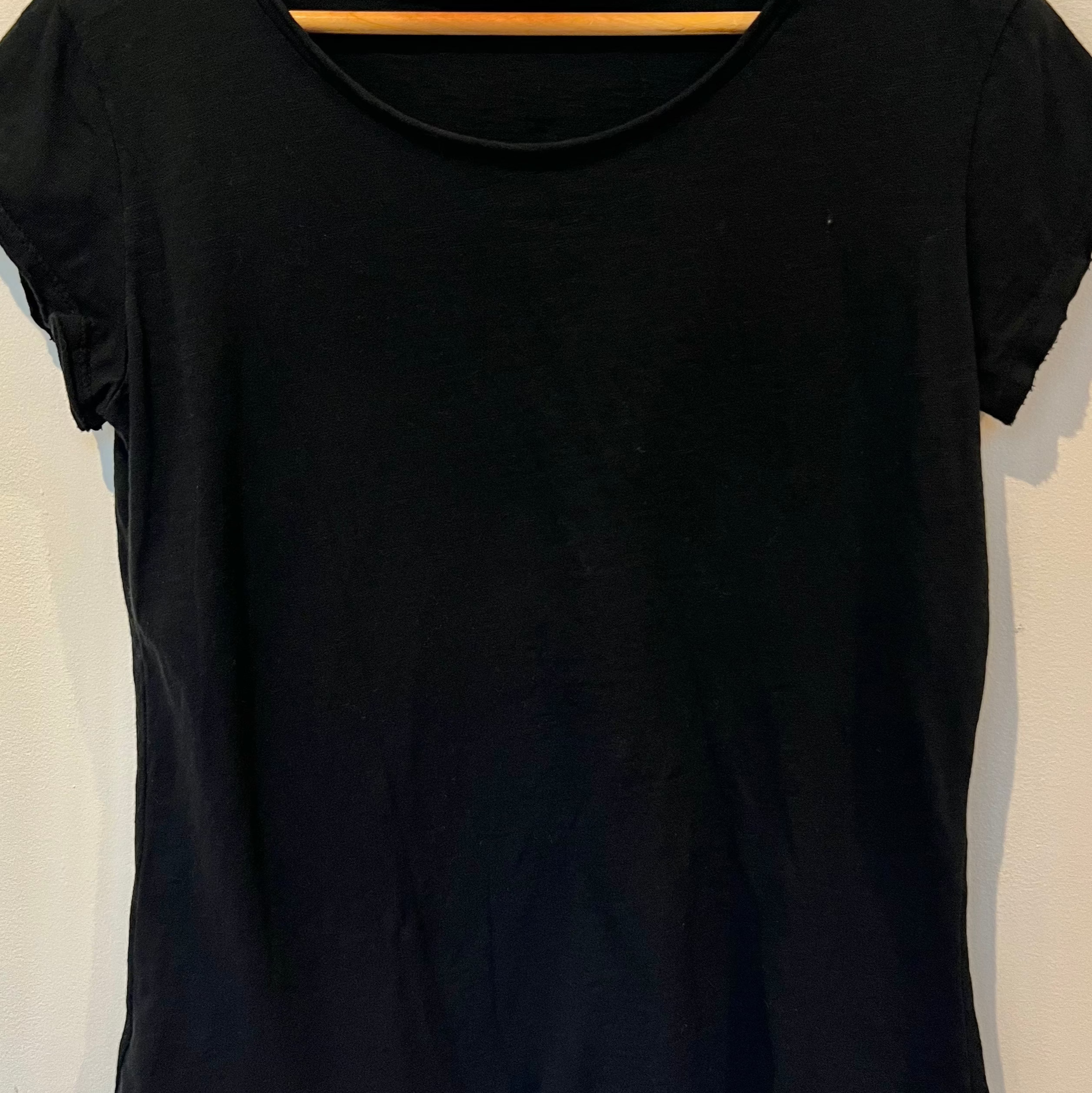 Black t-shirt on a wooden hanger against a white wall