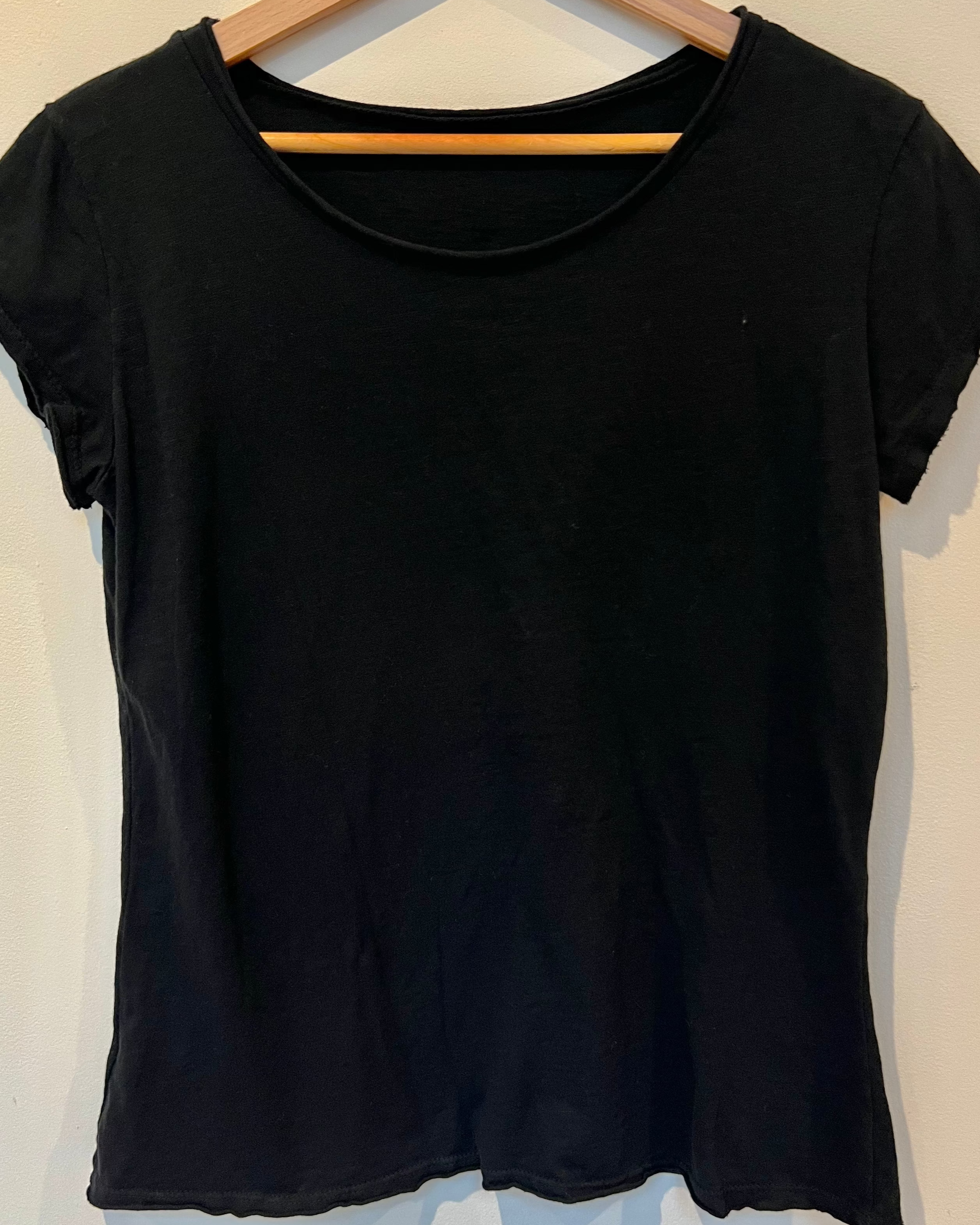 Black t-shirt on a wooden hanger against a white wall