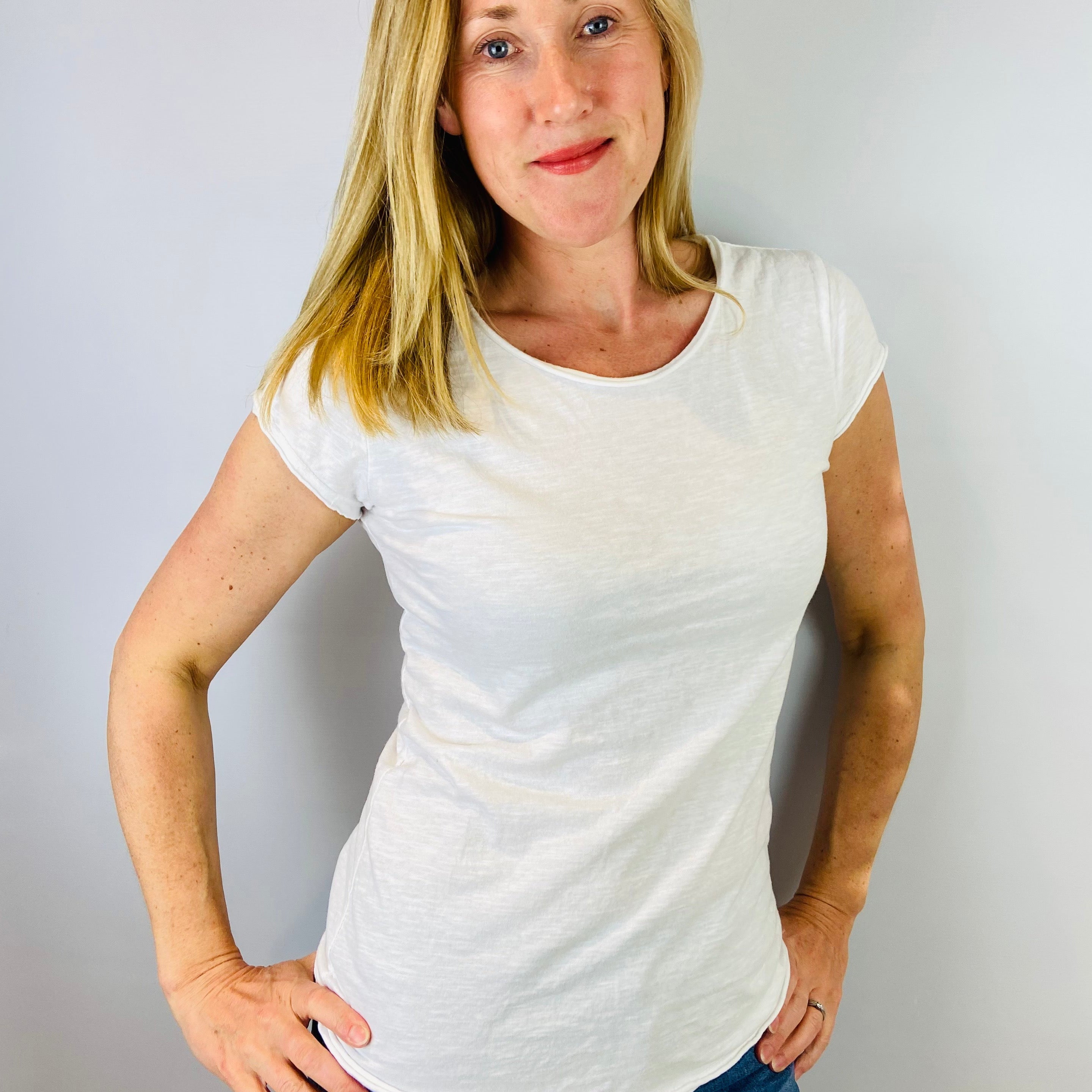 Woman wearing a white t-shirt and blue jeans against a plain background