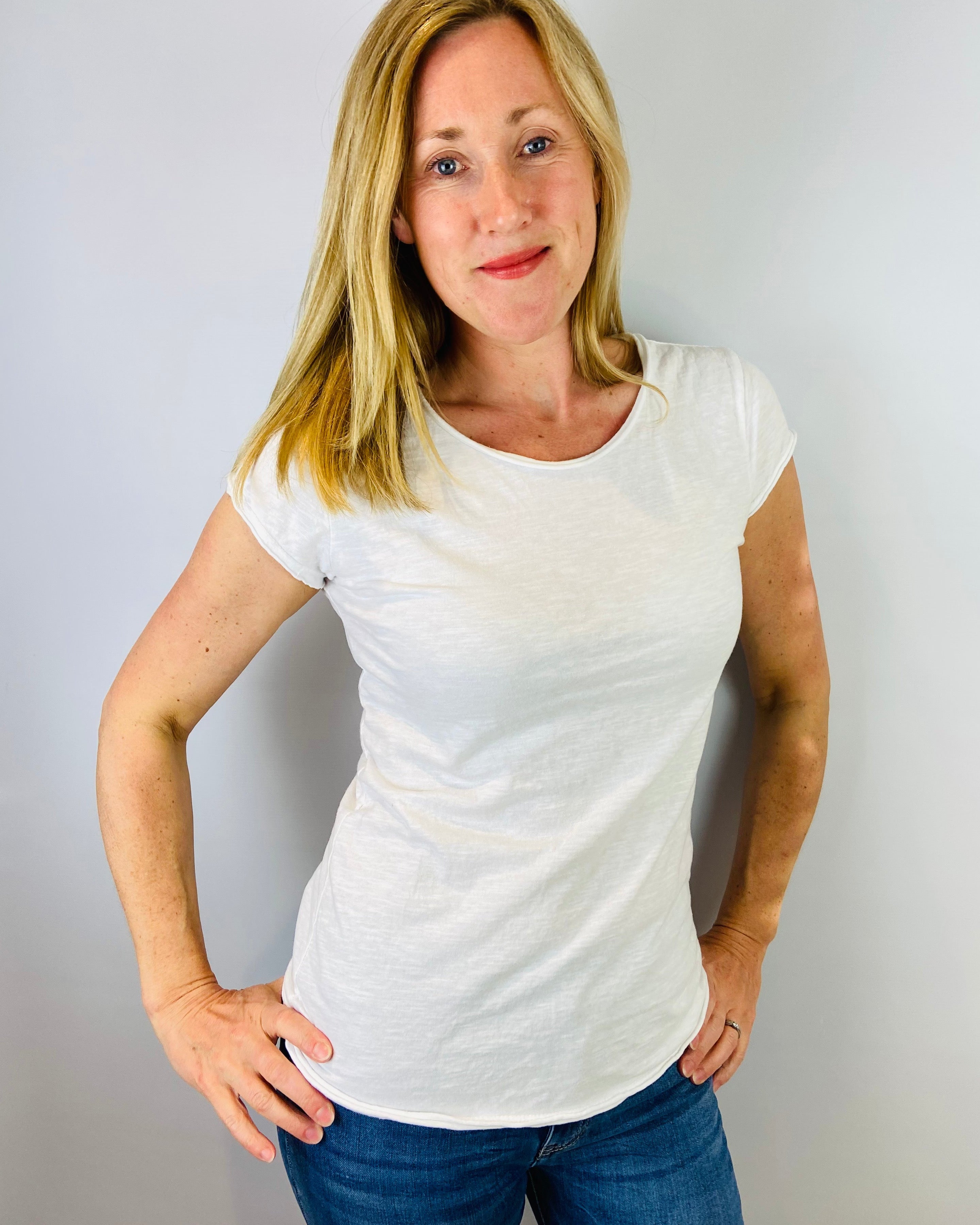 Woman wearing a white t-shirt and blue jeans against a plain background