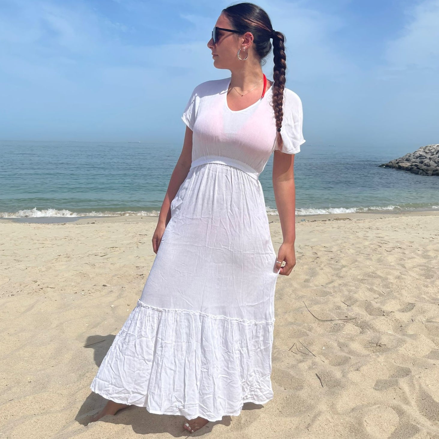 Woman in a white dress standing on a beach with ocean and sky in the background