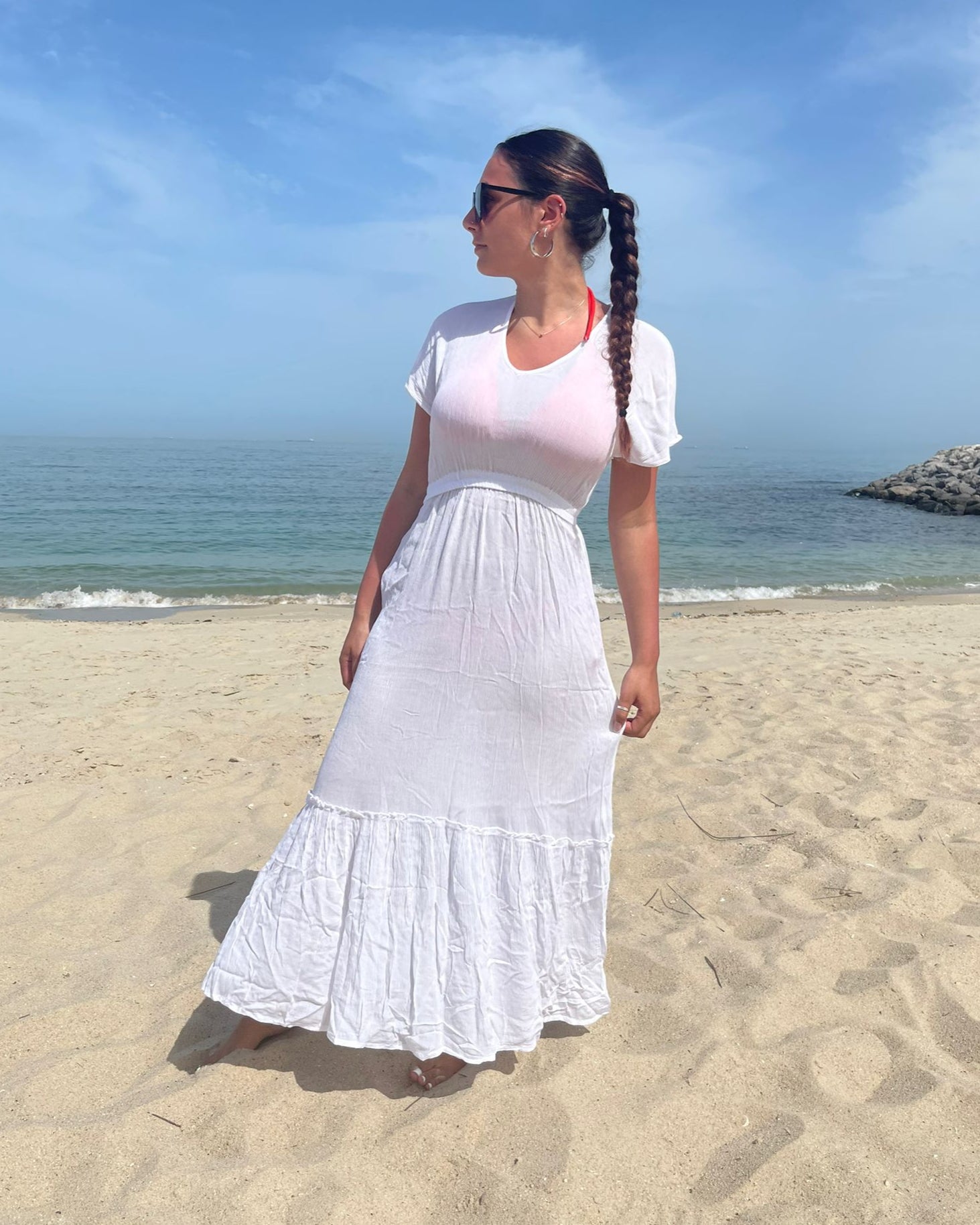 Woman in a white dress standing on a beach with ocean and sky in the background