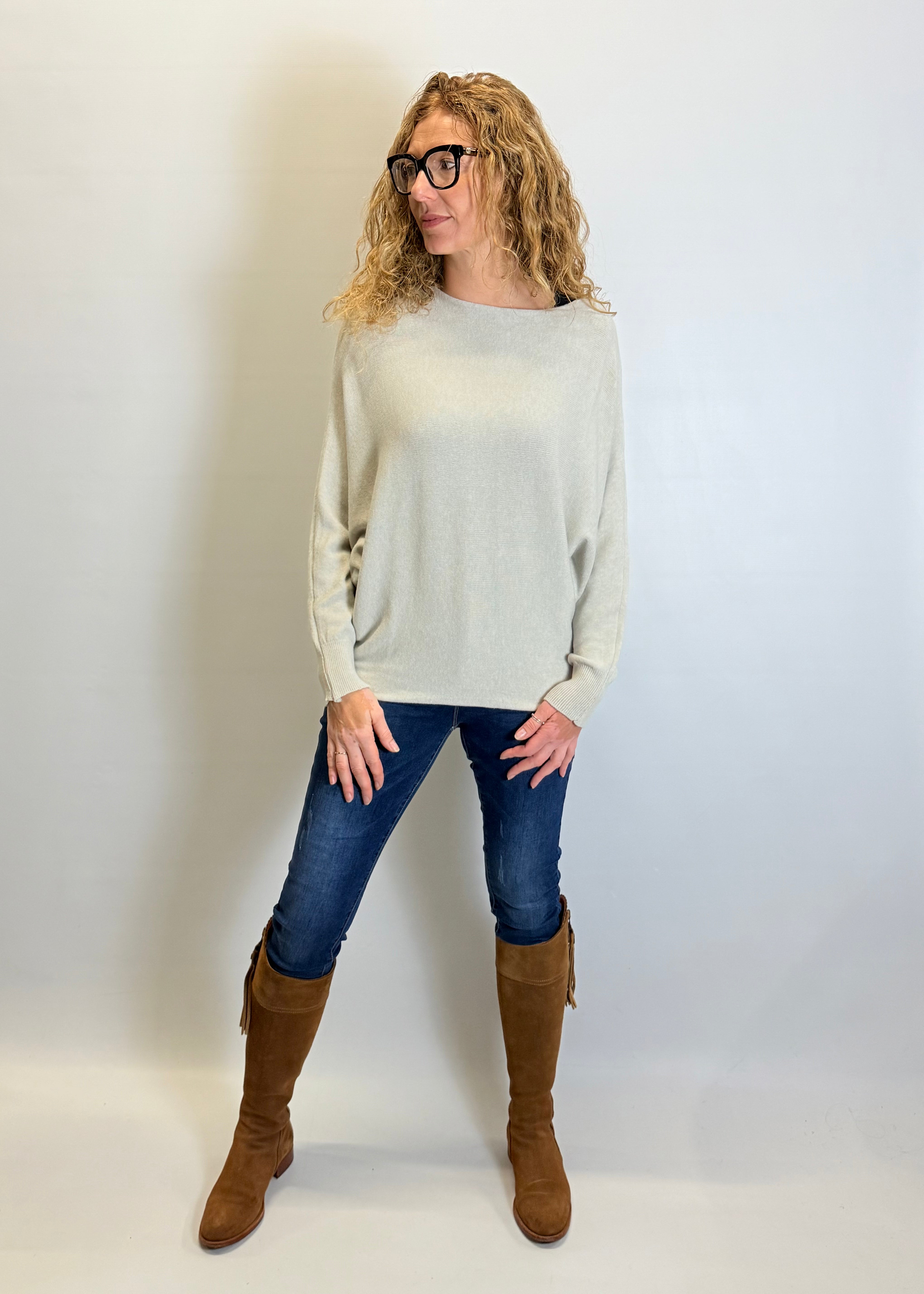 Woman wearing a light gray sweater, blue jeans, and brown knee-high boots against a white background