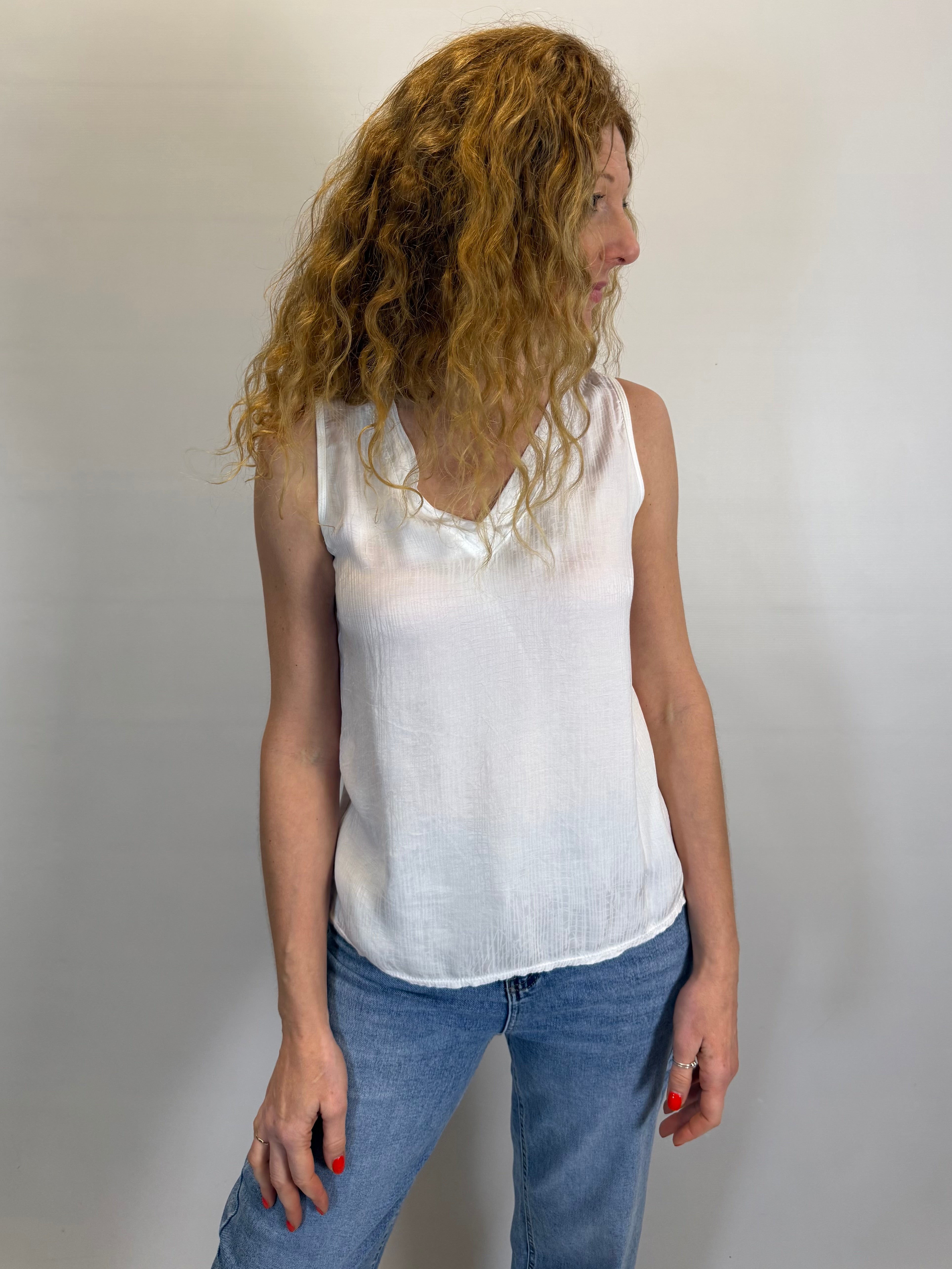 Woman wearing a white sleeveless top and blue jeans against a plain background