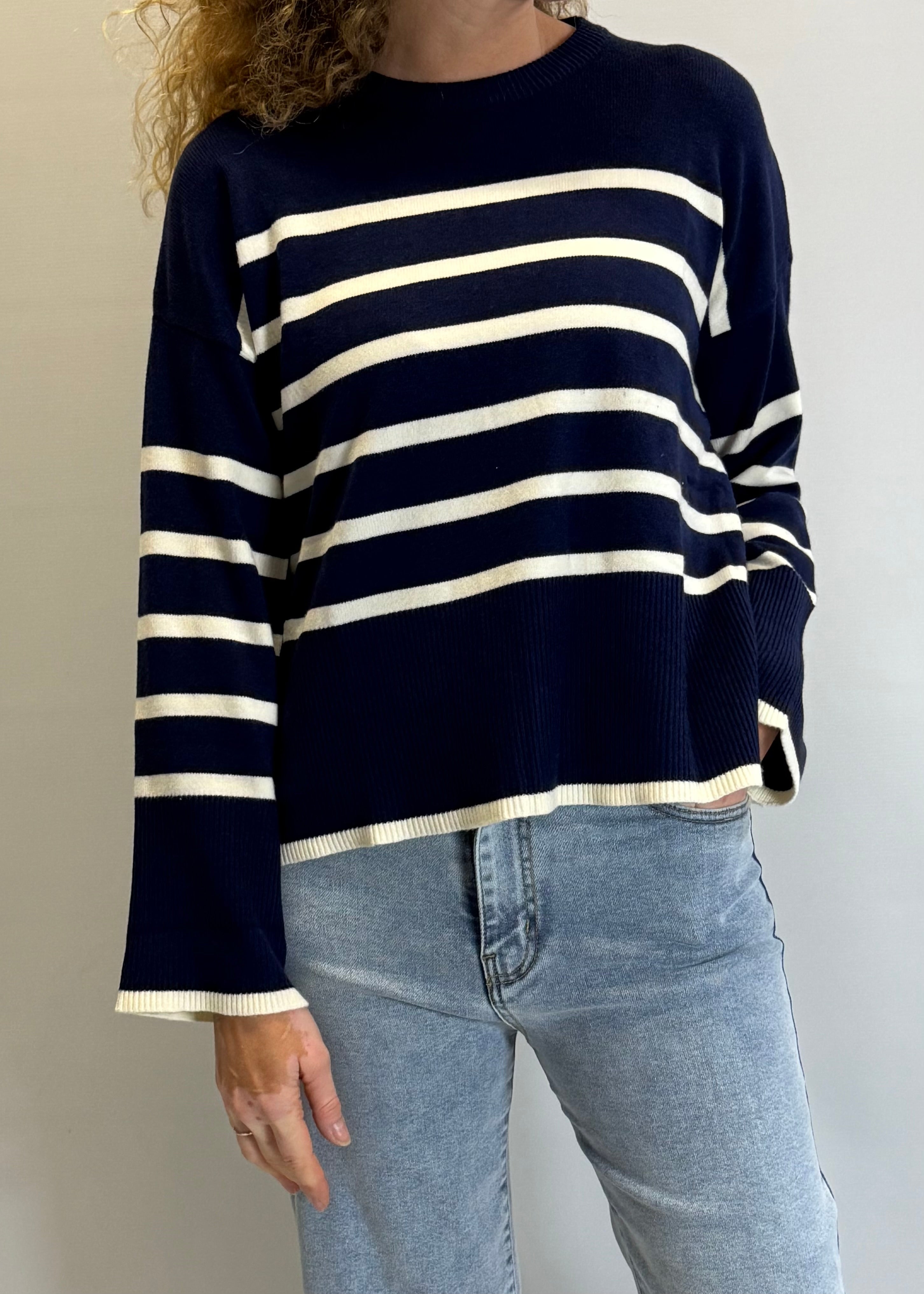 Person wearing a navy and white striped sweater with blue jeans against a plain background