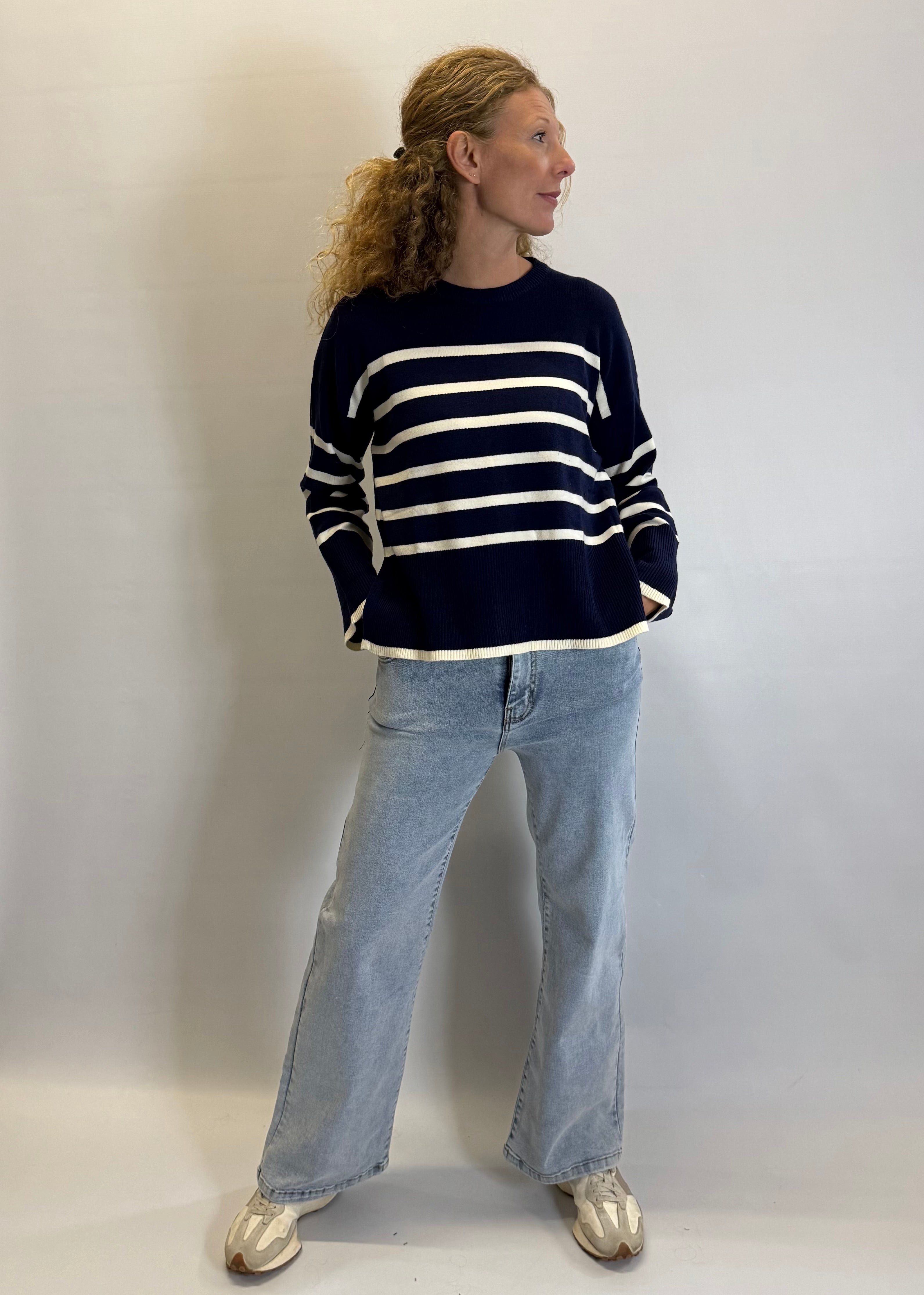 Person wearing a navy and white striped sweater with light blue jeans against a plain background