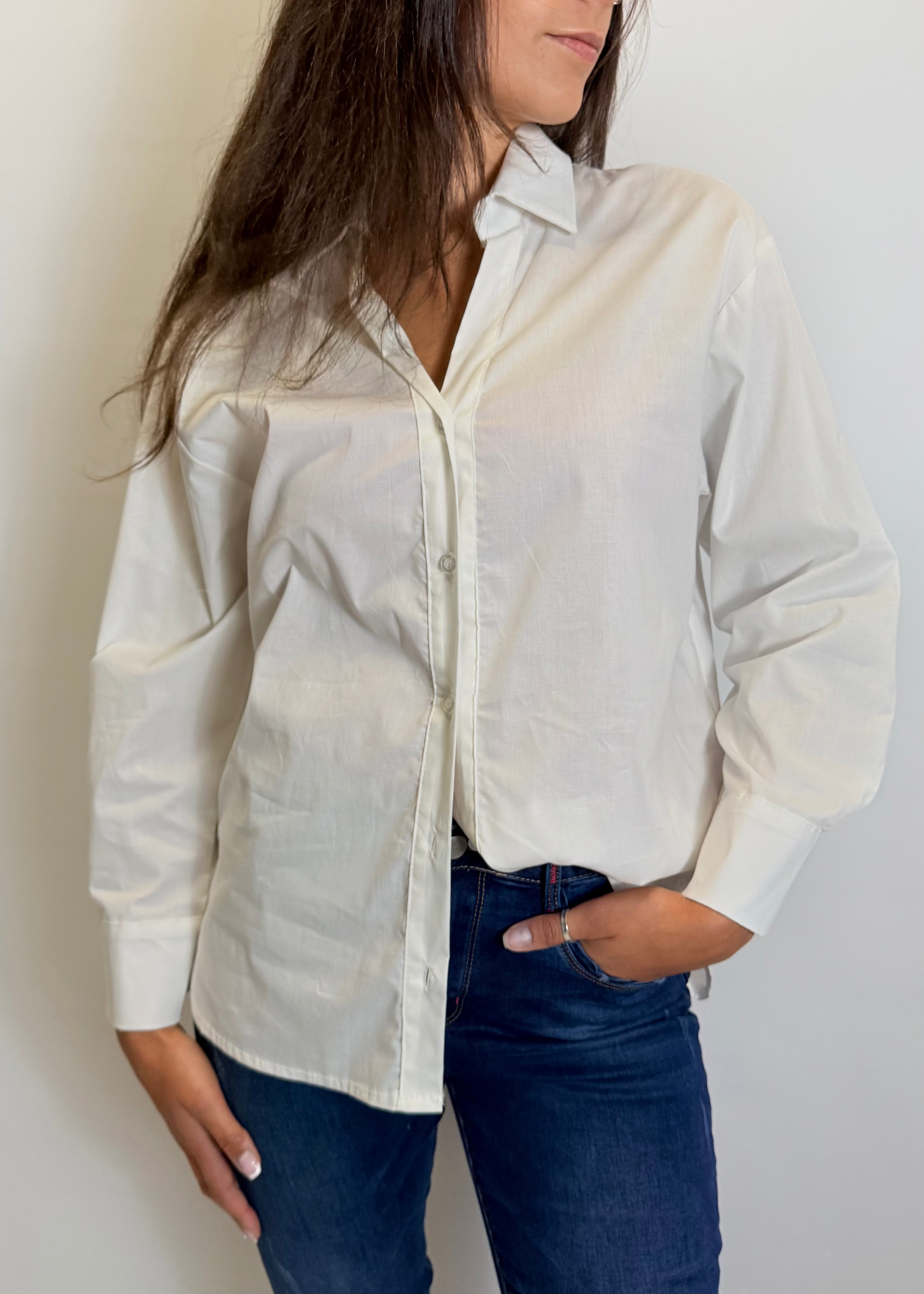 Person wearing a light-colored button-up shirt and dark jeans against a plain background