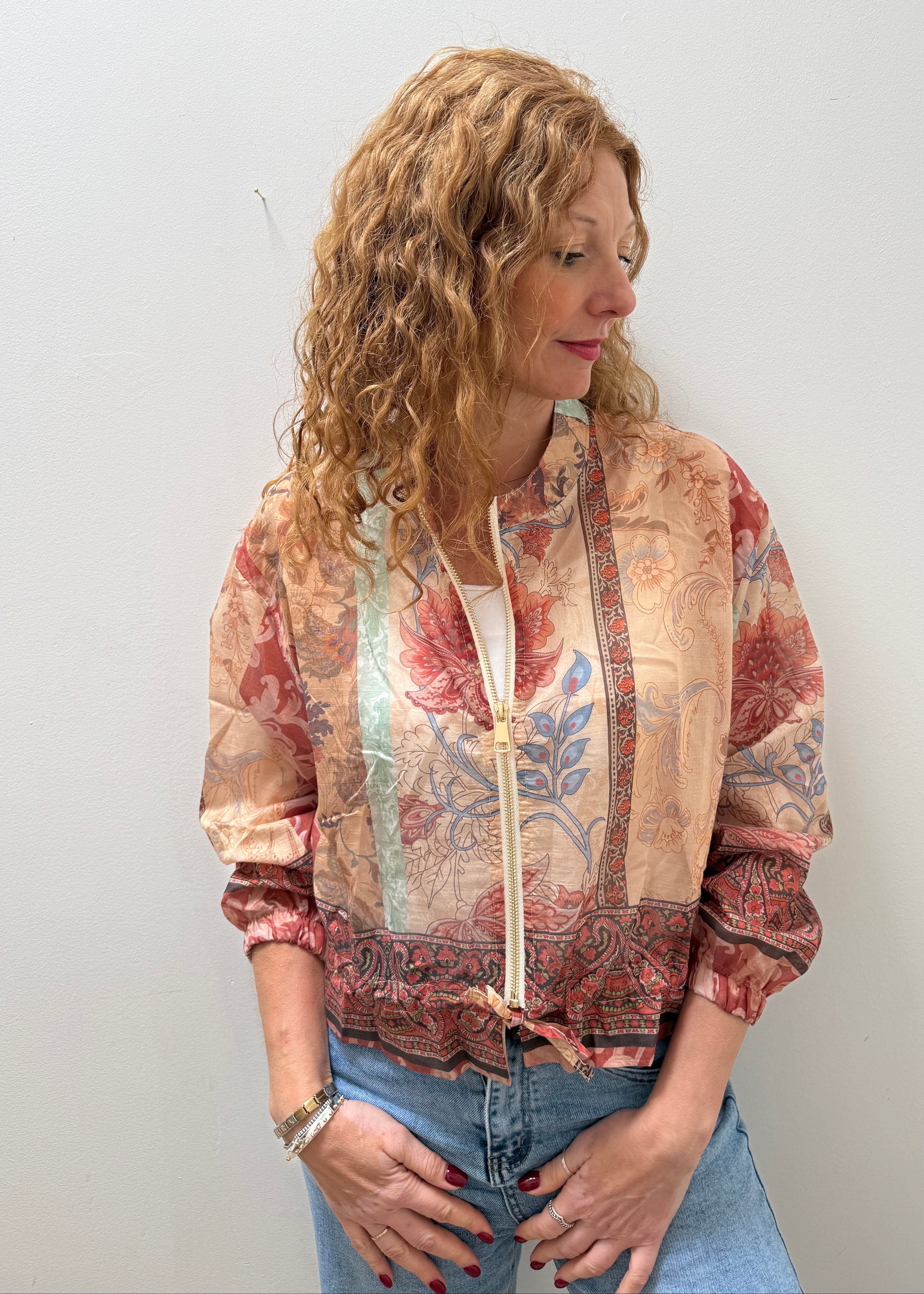 Woman wearing a patterned jacket and jeans against a plain background