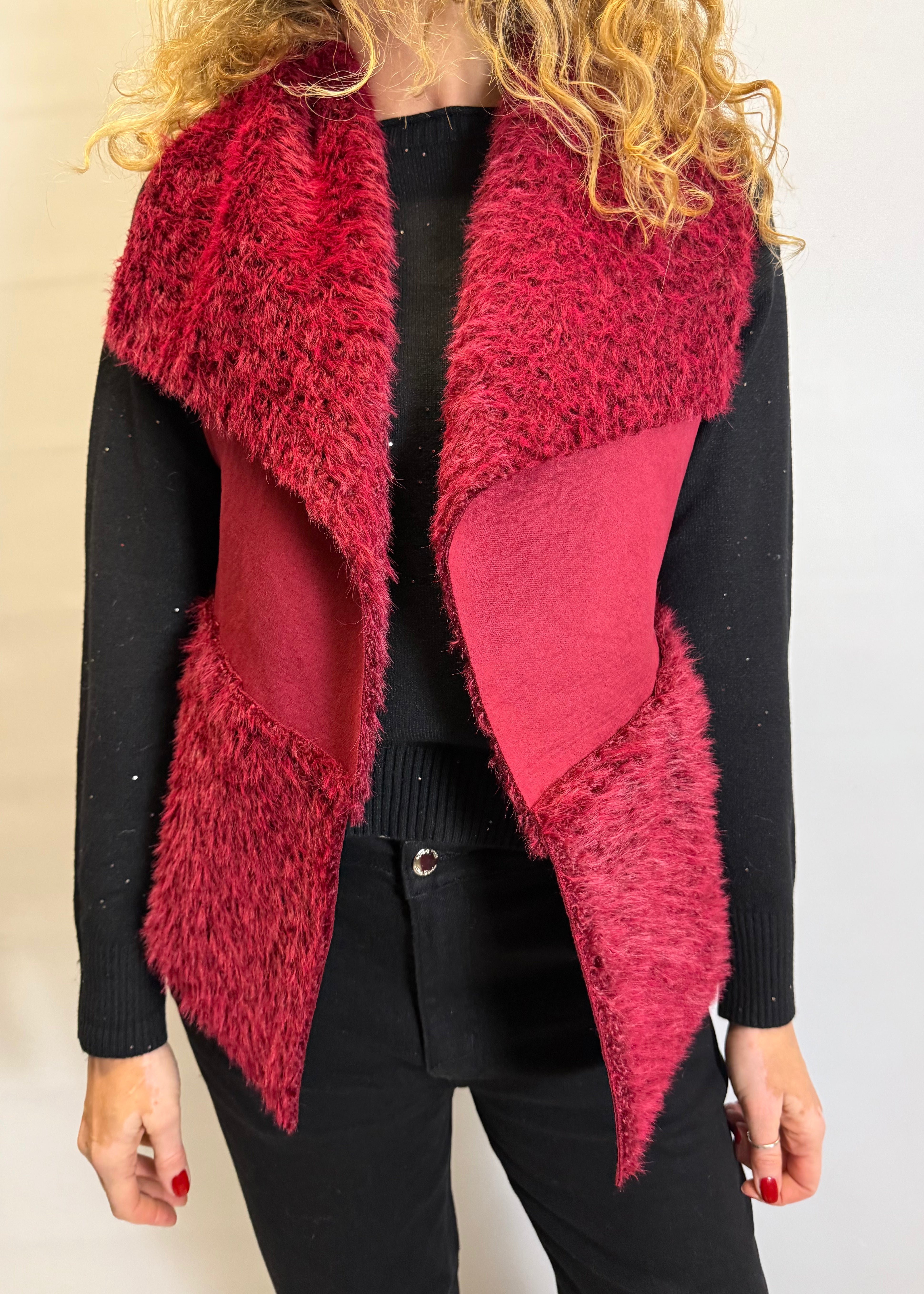 Person wearing a red furry vest over a black outfit against a plain background