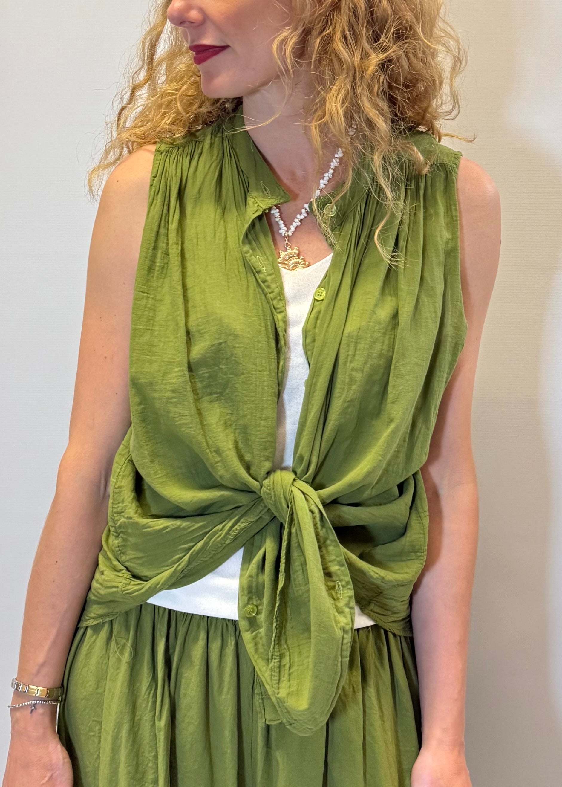 Woman wearing a green sleeveless top with a knot detail over a white shirt.