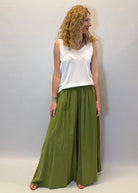 Woman wearing a white top and green wide-leg pants against a plain background
