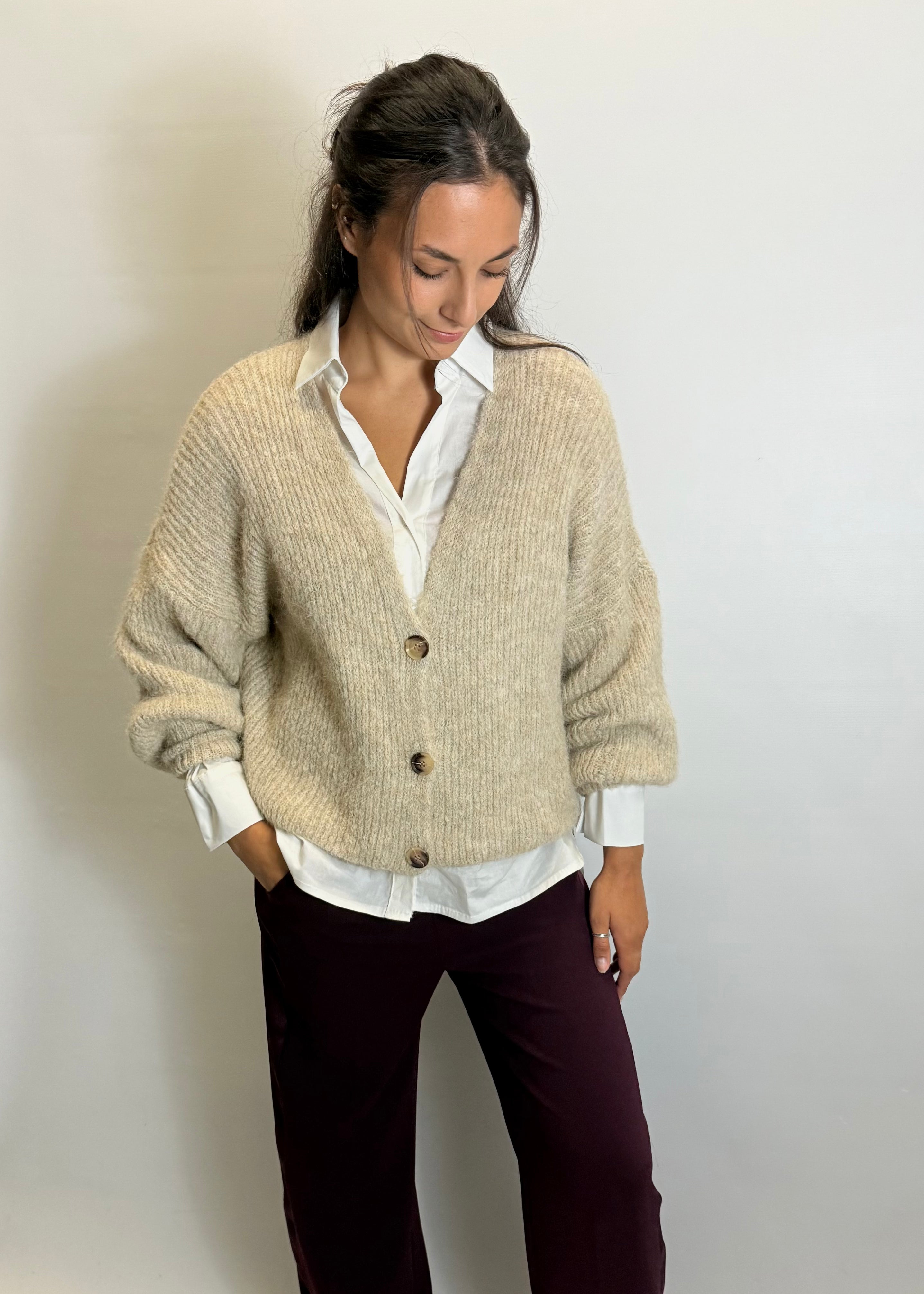 Woman wearing a beige cardigan over a white shirt with a plain background