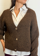 Person wearing a brown cardigan over a white shirt with a neutral background