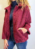 Person wearing a red textured jacket with buttons on a plain background