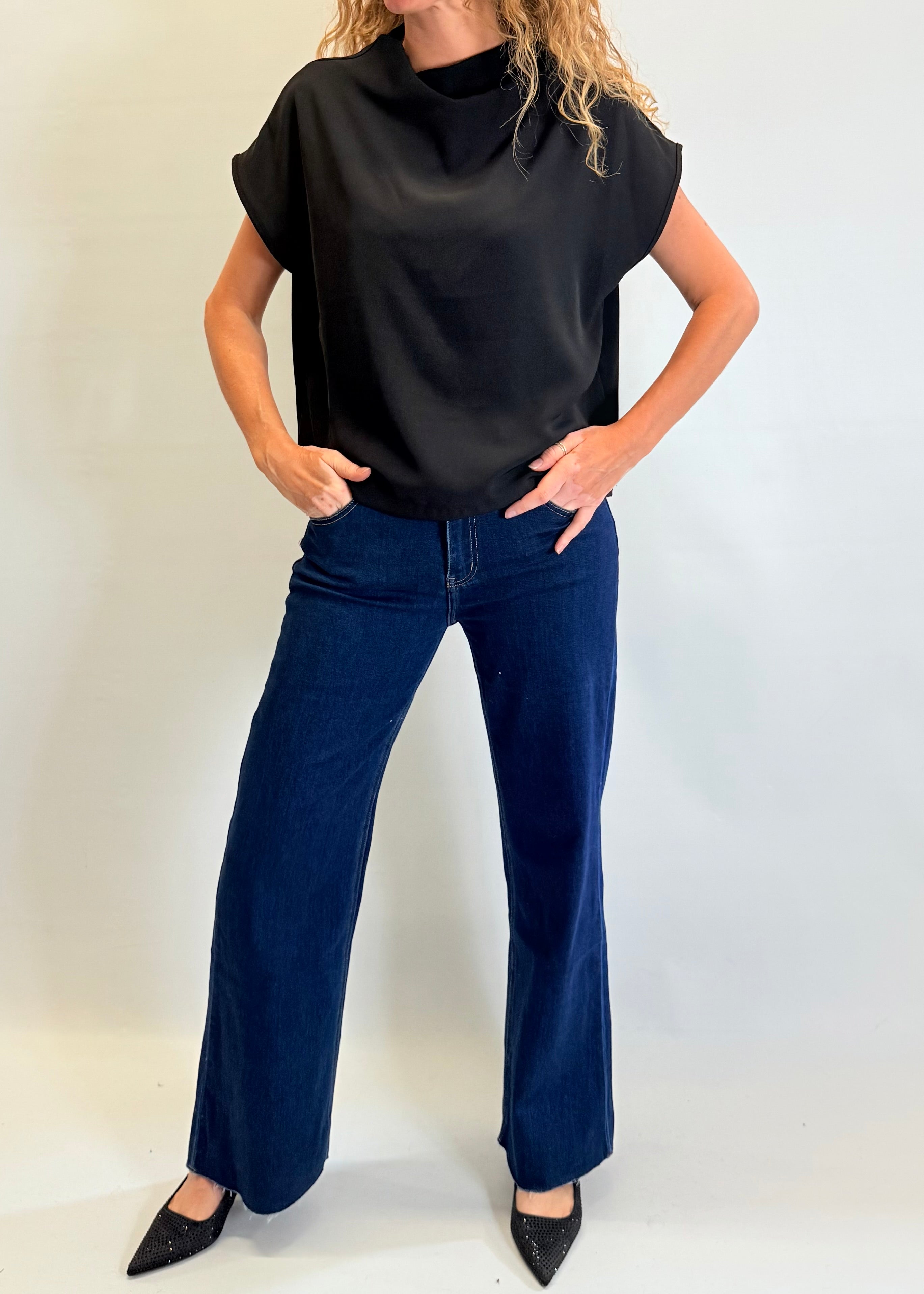 Person wearing a black sleeveless top and blue jeans against a white background