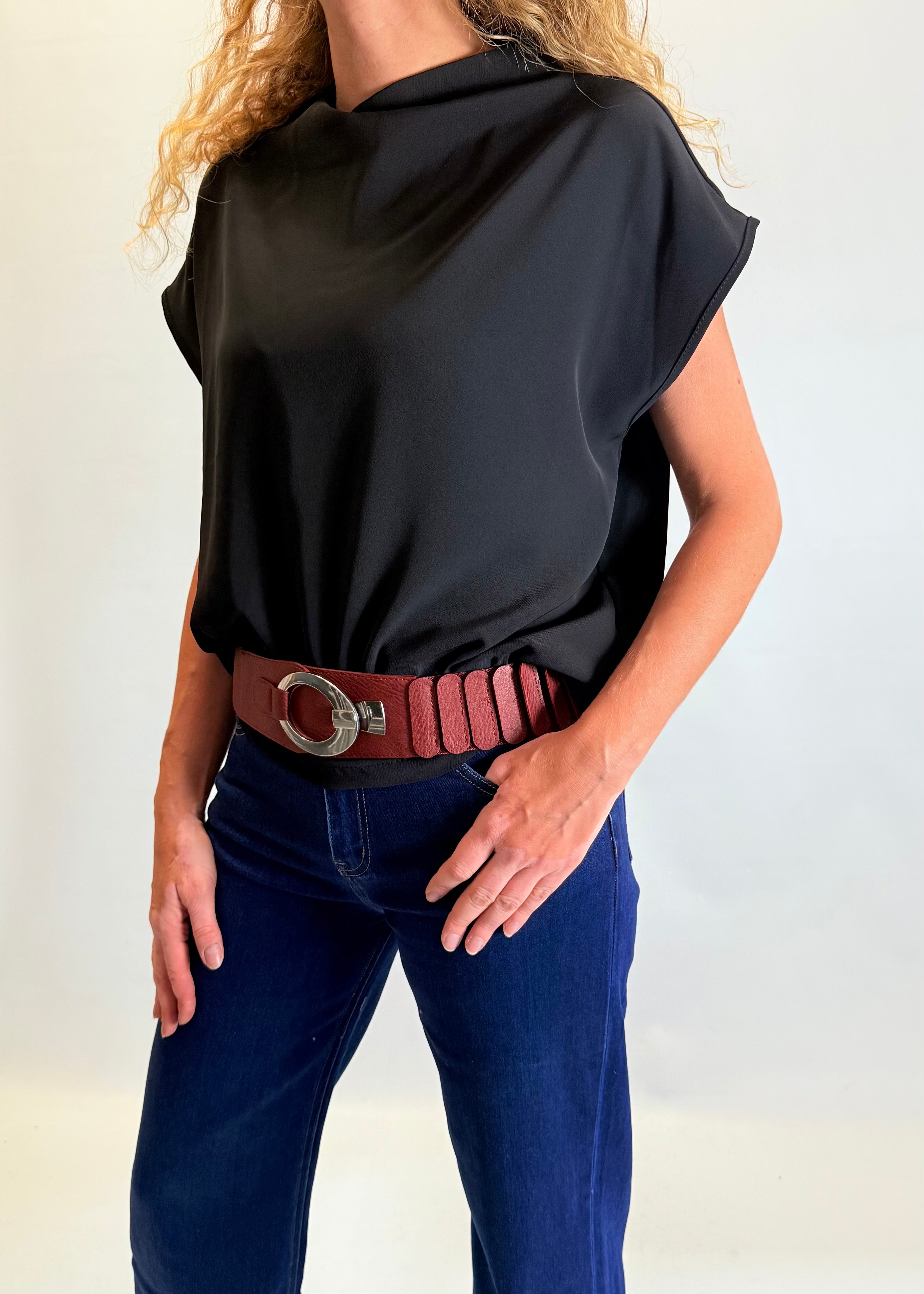 Person wearing a black sleeveless top and blue jeans with a brown belt against a white background