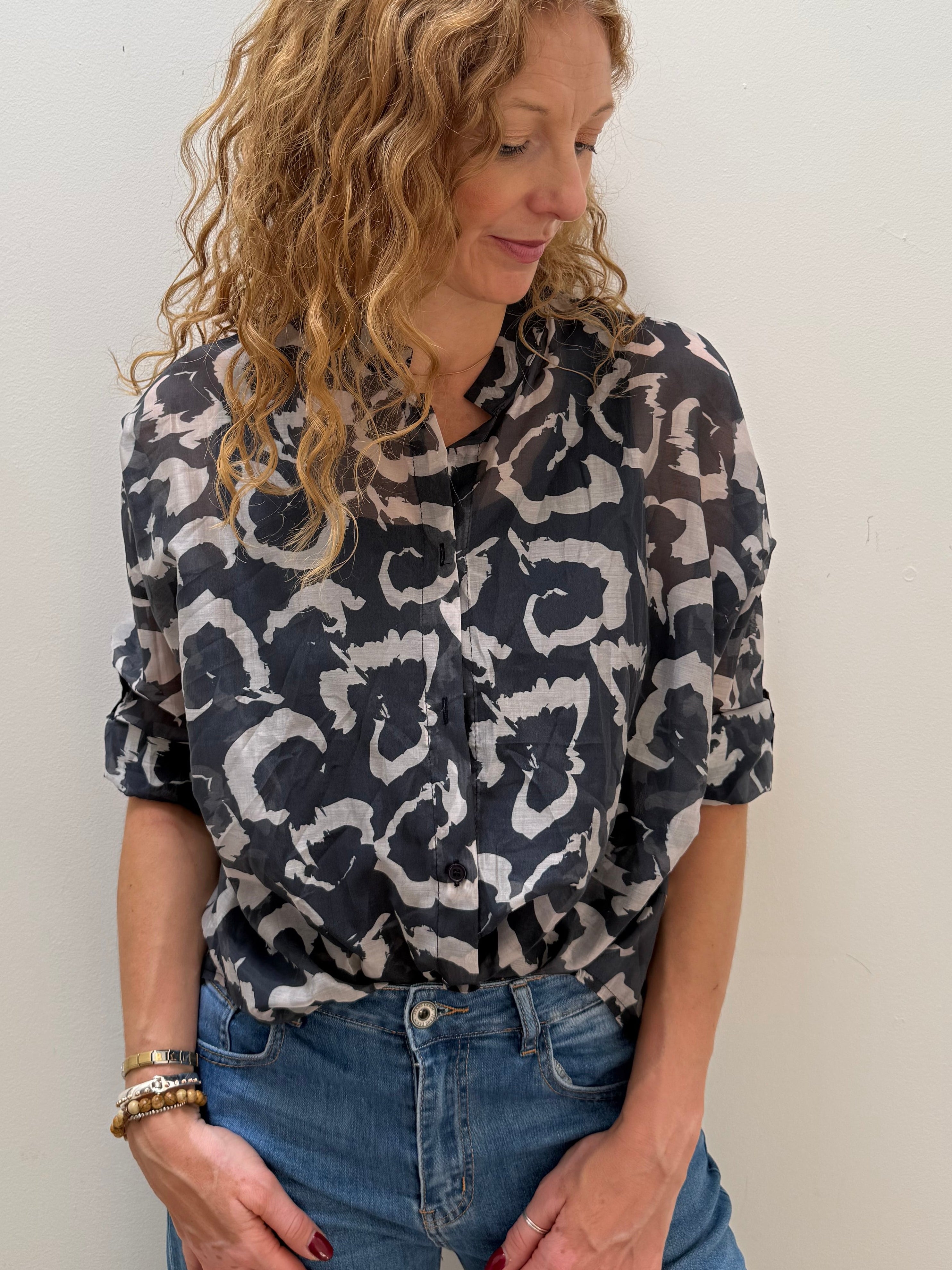 Woman wearing a patterned shirt and jeans against a white wall