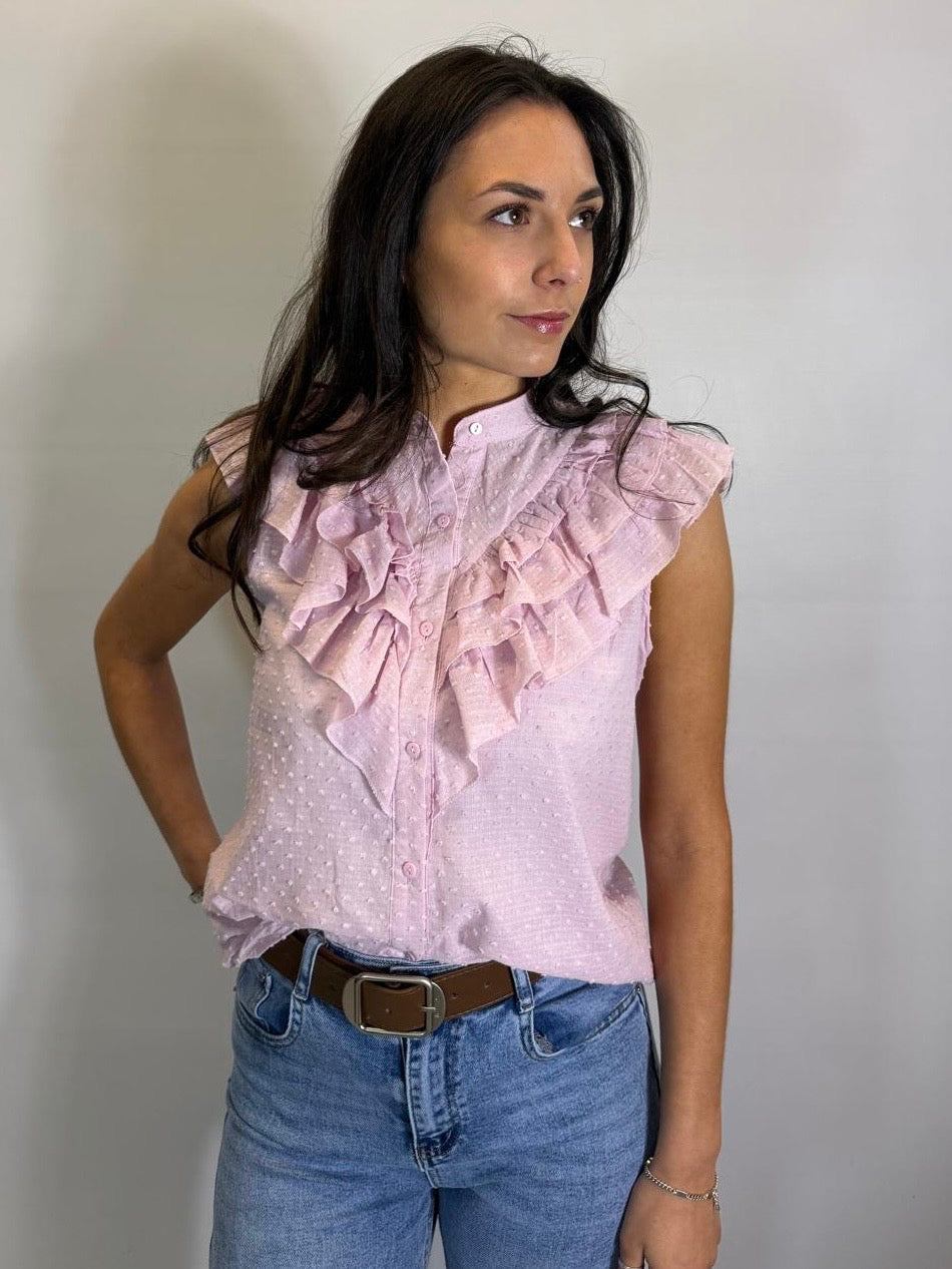 Woman wearing a light pink blouse with ruffles and blue jeans against a plain background